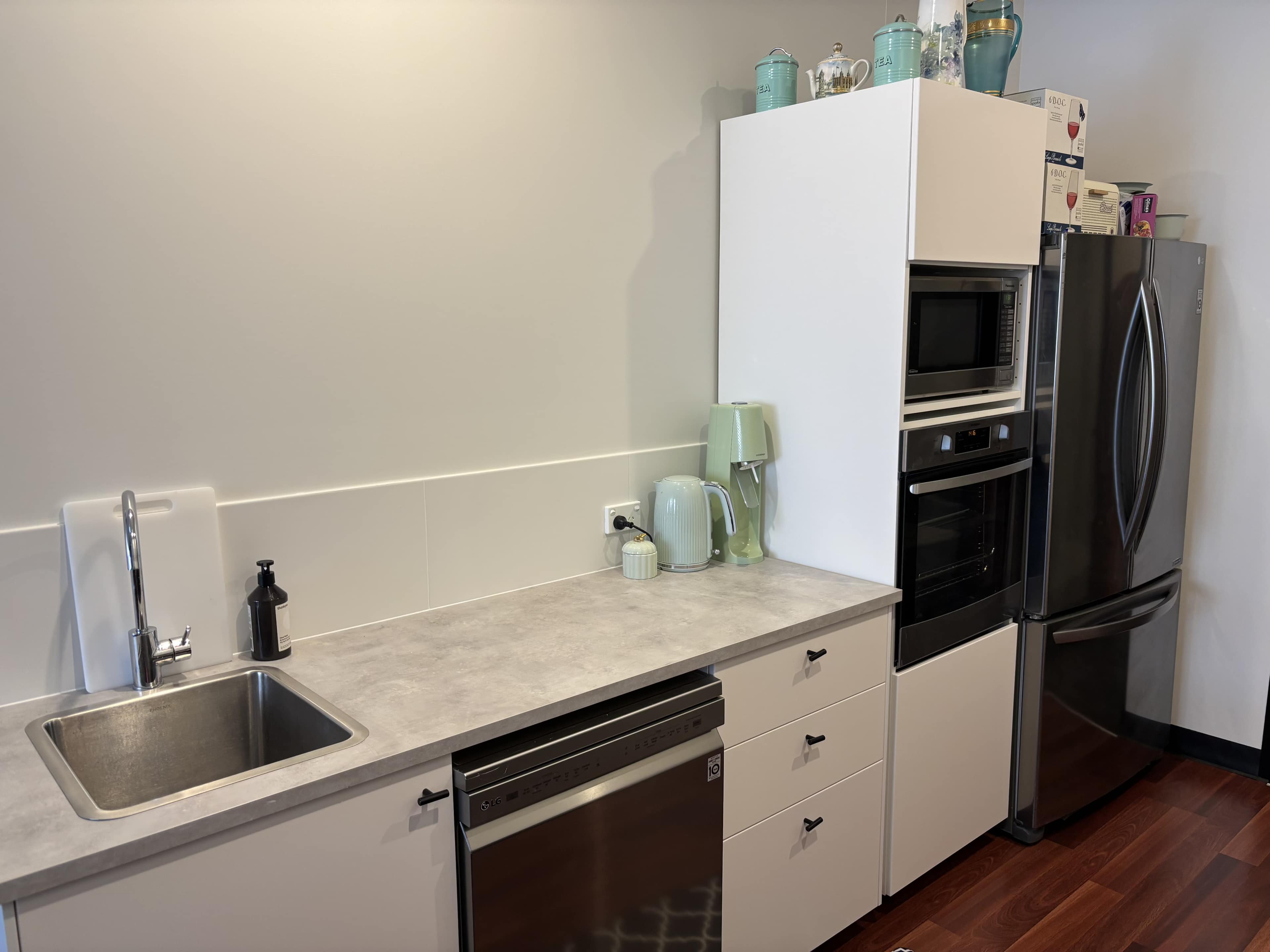 The image shows a modern kitchen with a stainless steel sink, countertop, built-in oven and microwave, and a refrigerator, all arranged along a wall with light-colored cabinetry.