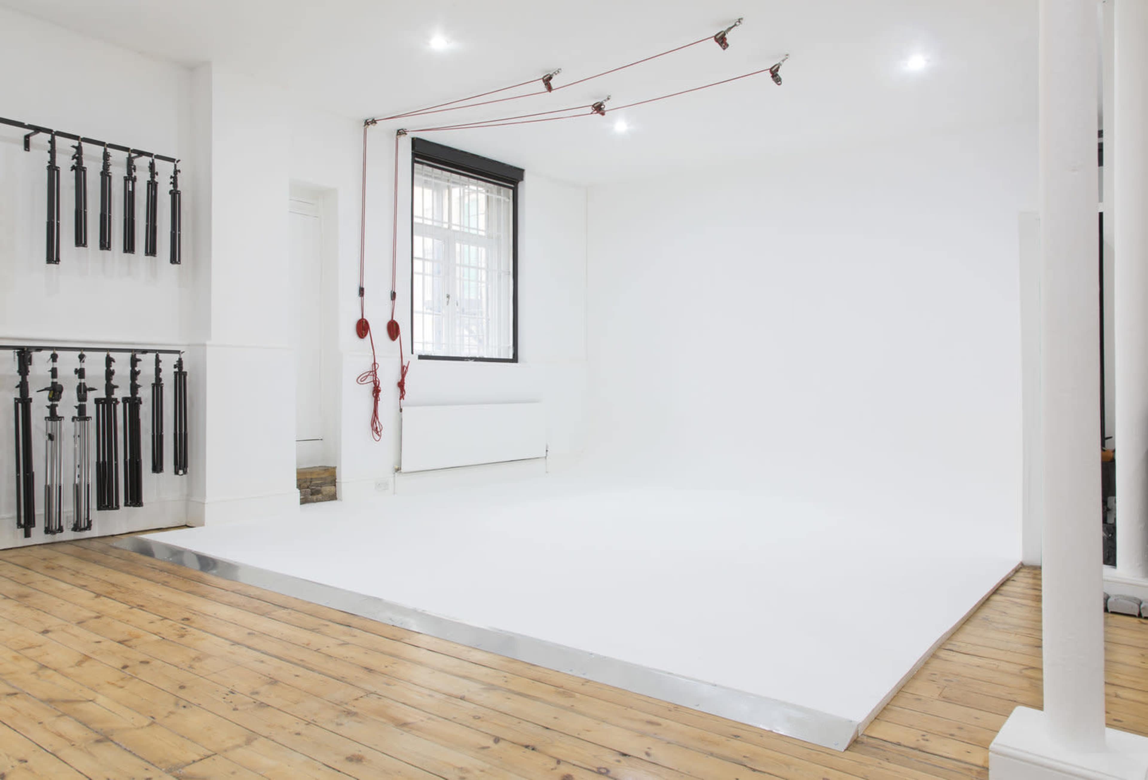 A white studio space with a wooden floor, equipped with various hanging props along one wall and a raised white platform in the center.