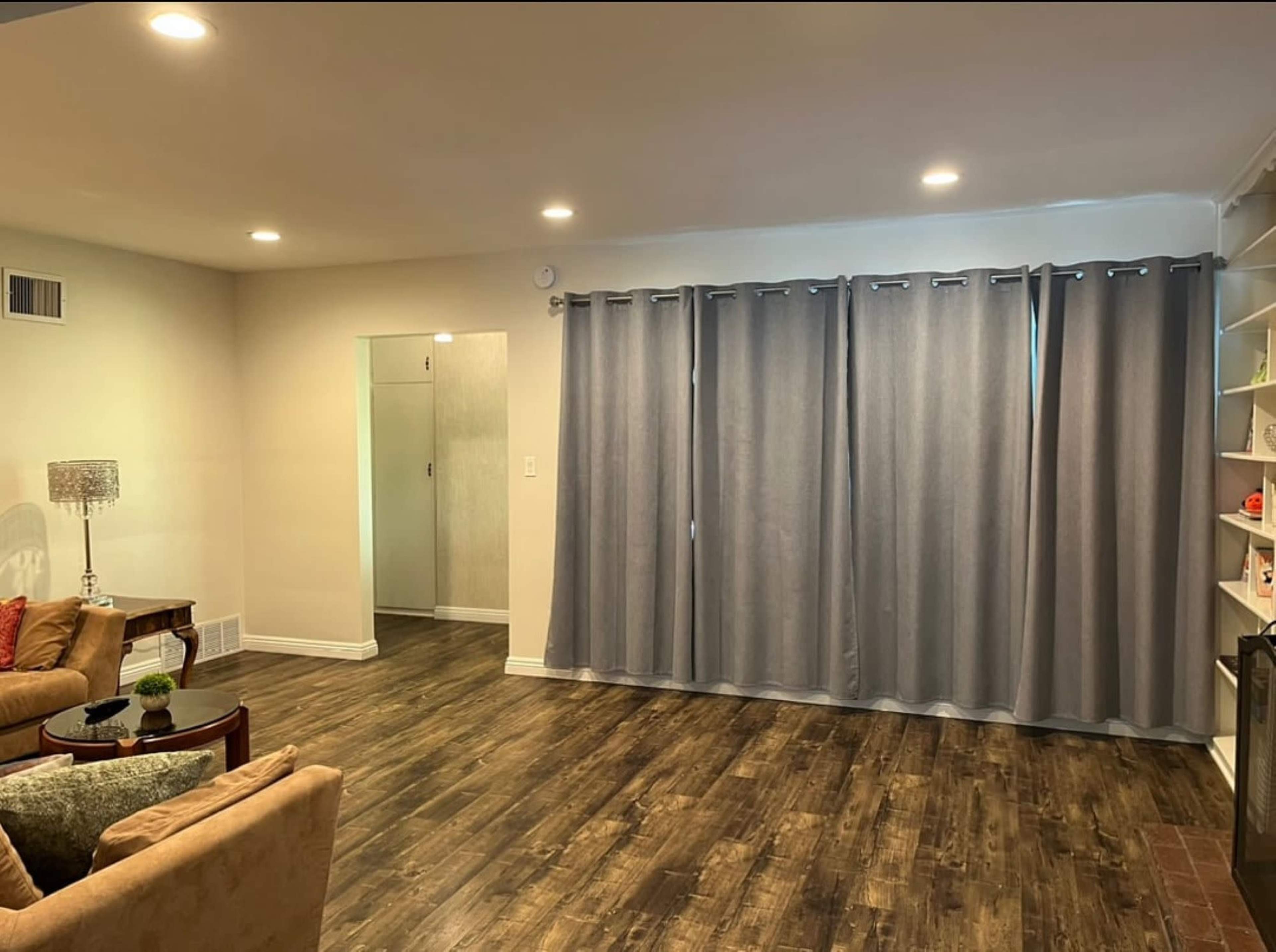 A spacious living room features a sofa, a round table, and a wall of gray curtains covering a doorway.