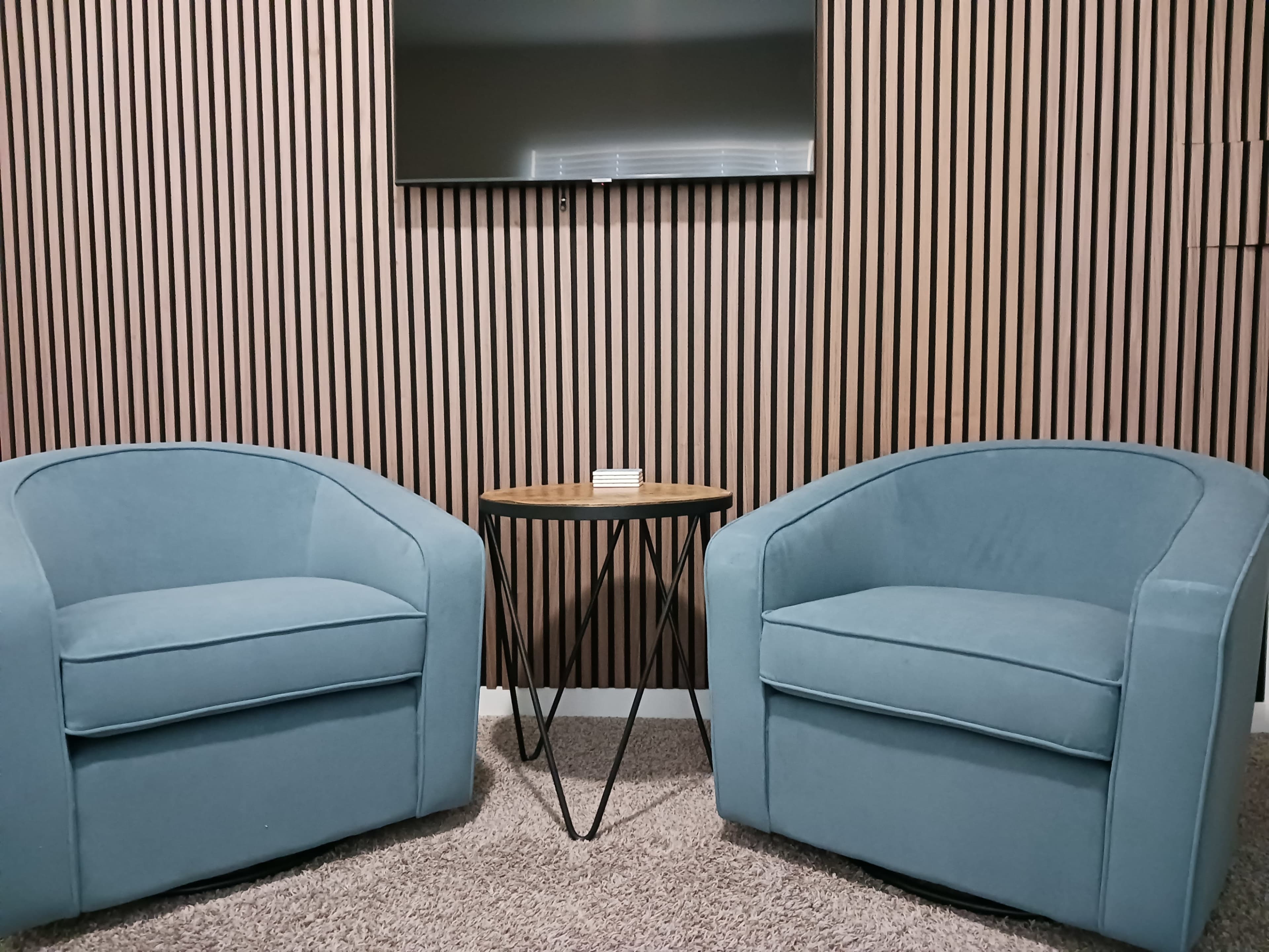 The image shows two light blue upholstered chairs facing each other across a small wooden table, set against a backdrop of vertical wooden slats.