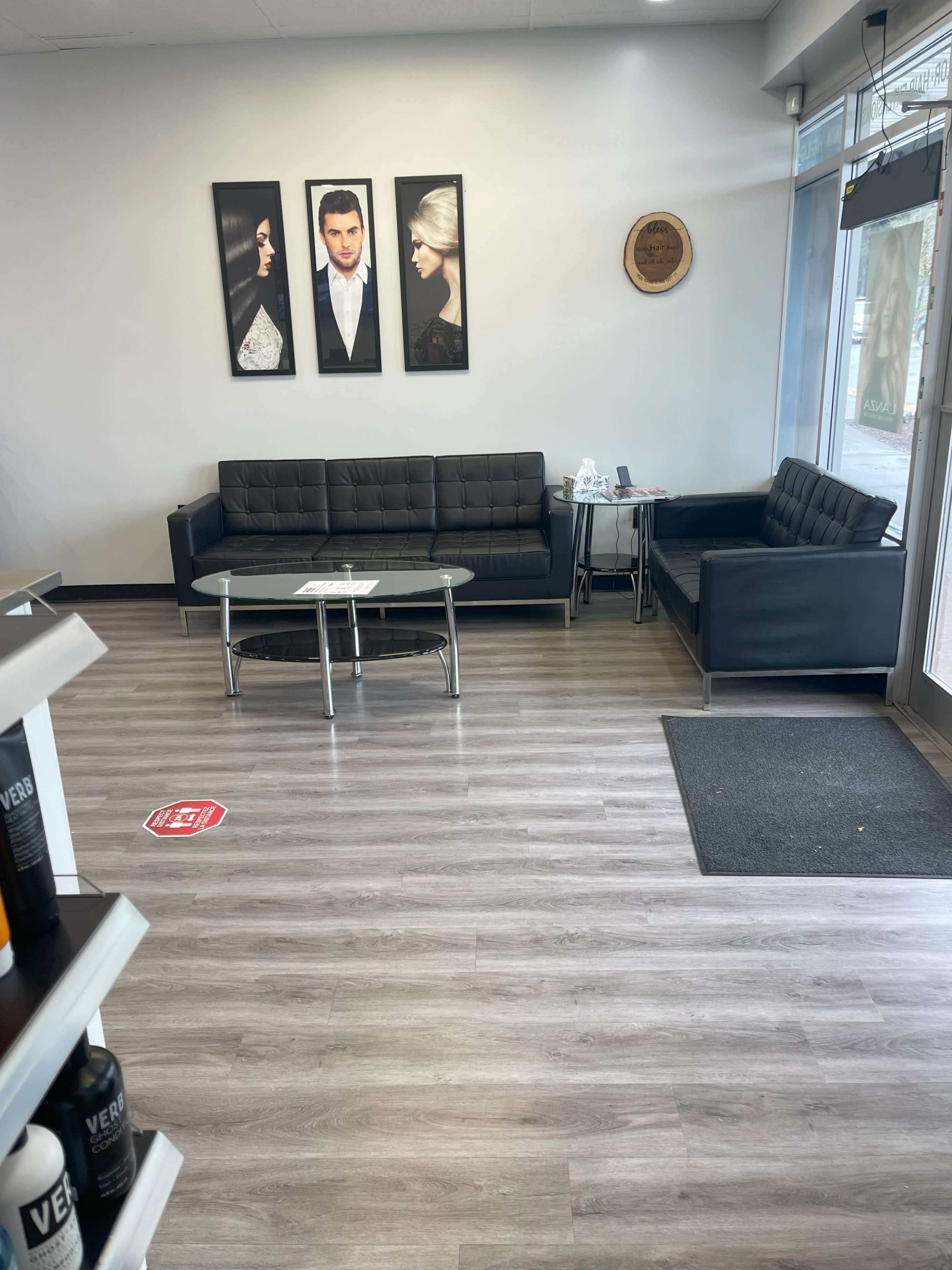 The image shows a modern waiting area with black sofas, a glass coffee table, and framed portraits on the wall.