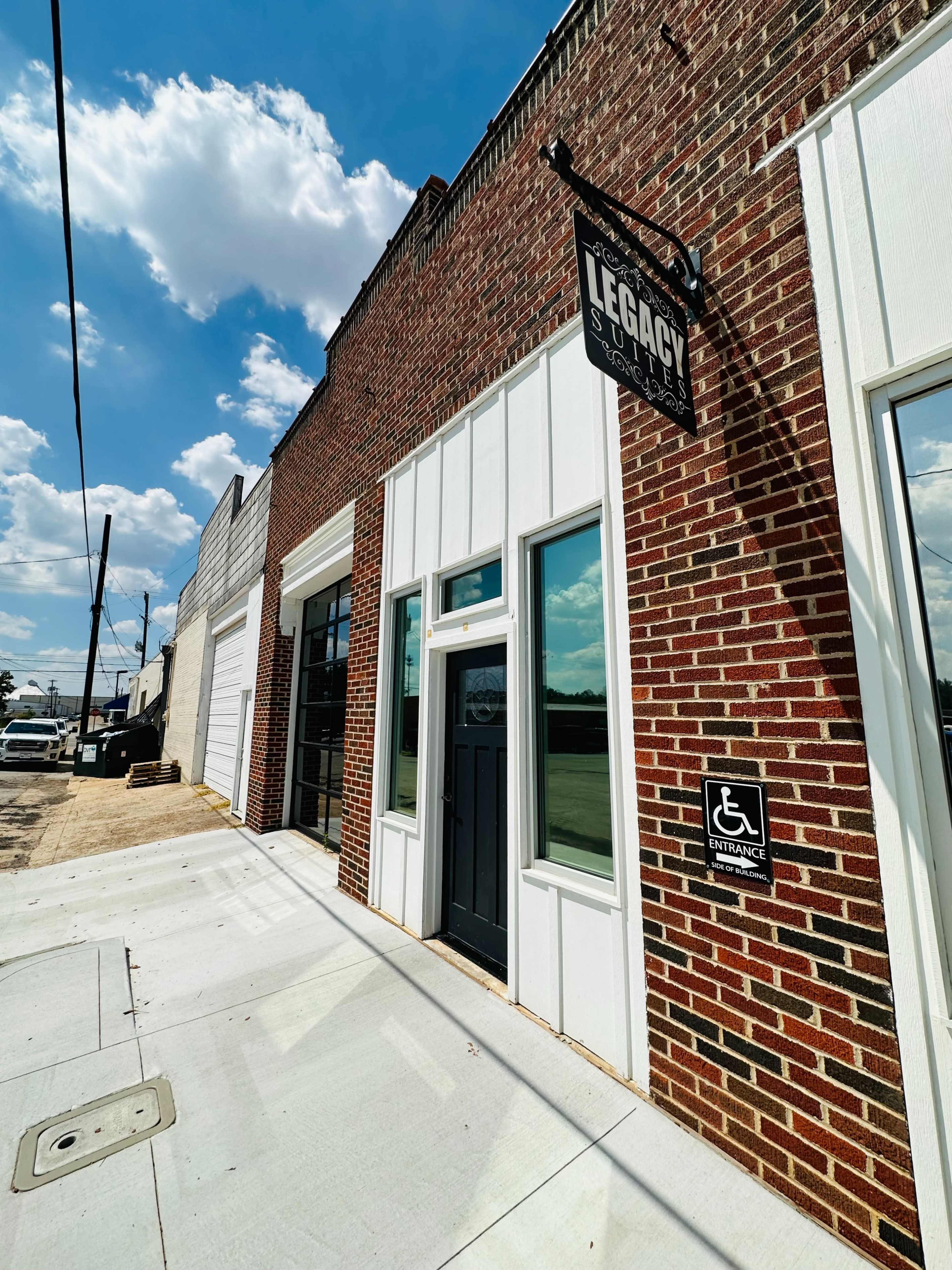 A brick storefront with large windows, a black door, and a sign reading "Legacy" above it, along with a handicap-accessible entrance sign.