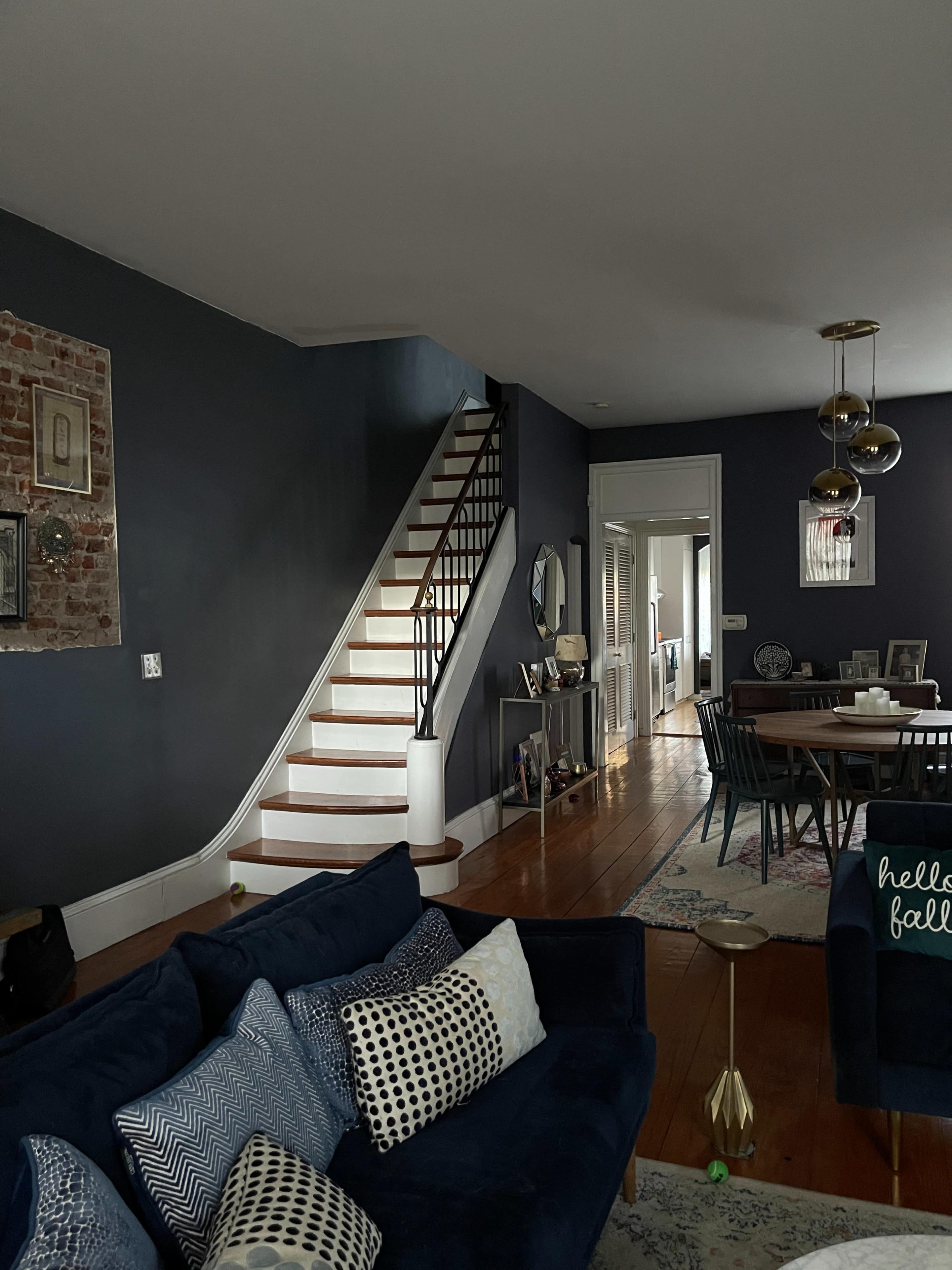 A modern living room featuring a dark blue wall, a staircase leading to an upper floor, and a dining area with a wooden table and chairs.