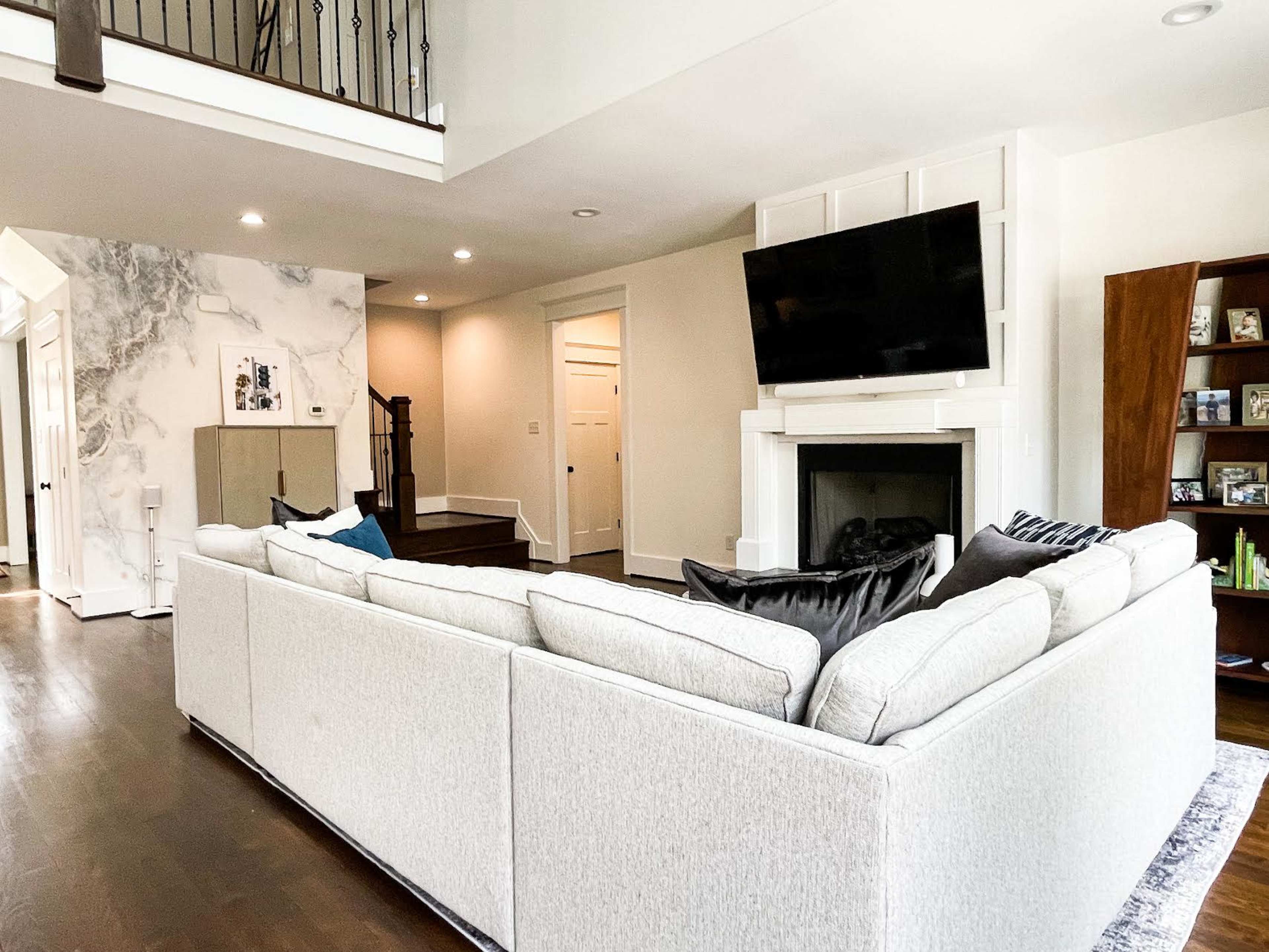 A spacious living room features a large sectional sofa facing a fireplace and a mounted television on the wall.