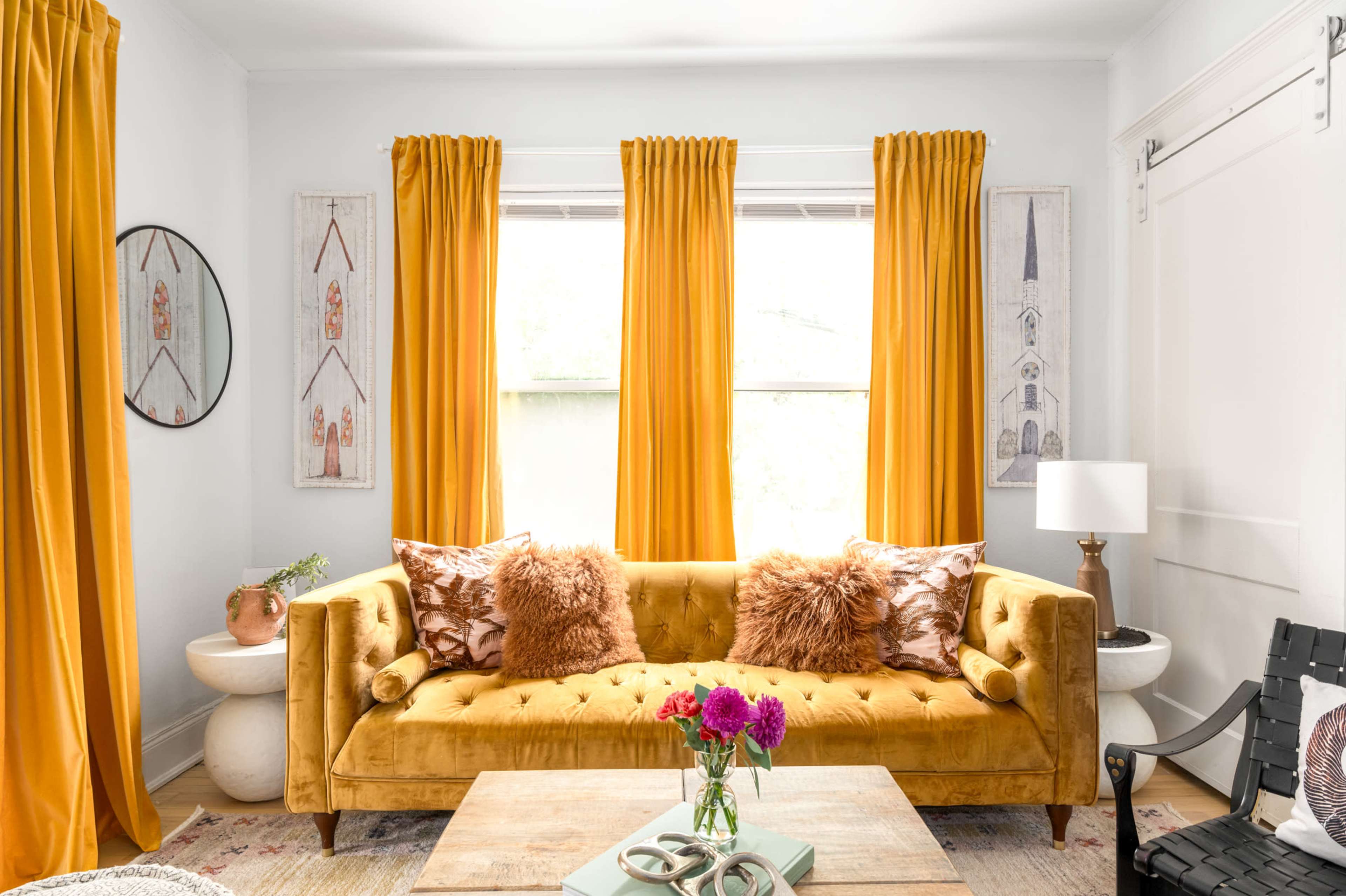The image features a bright living room with a yellow tufted sofa, adorned with decorative pillows, flanked by large yellow curtains and complemented by a wooden coffee table and a lamp.