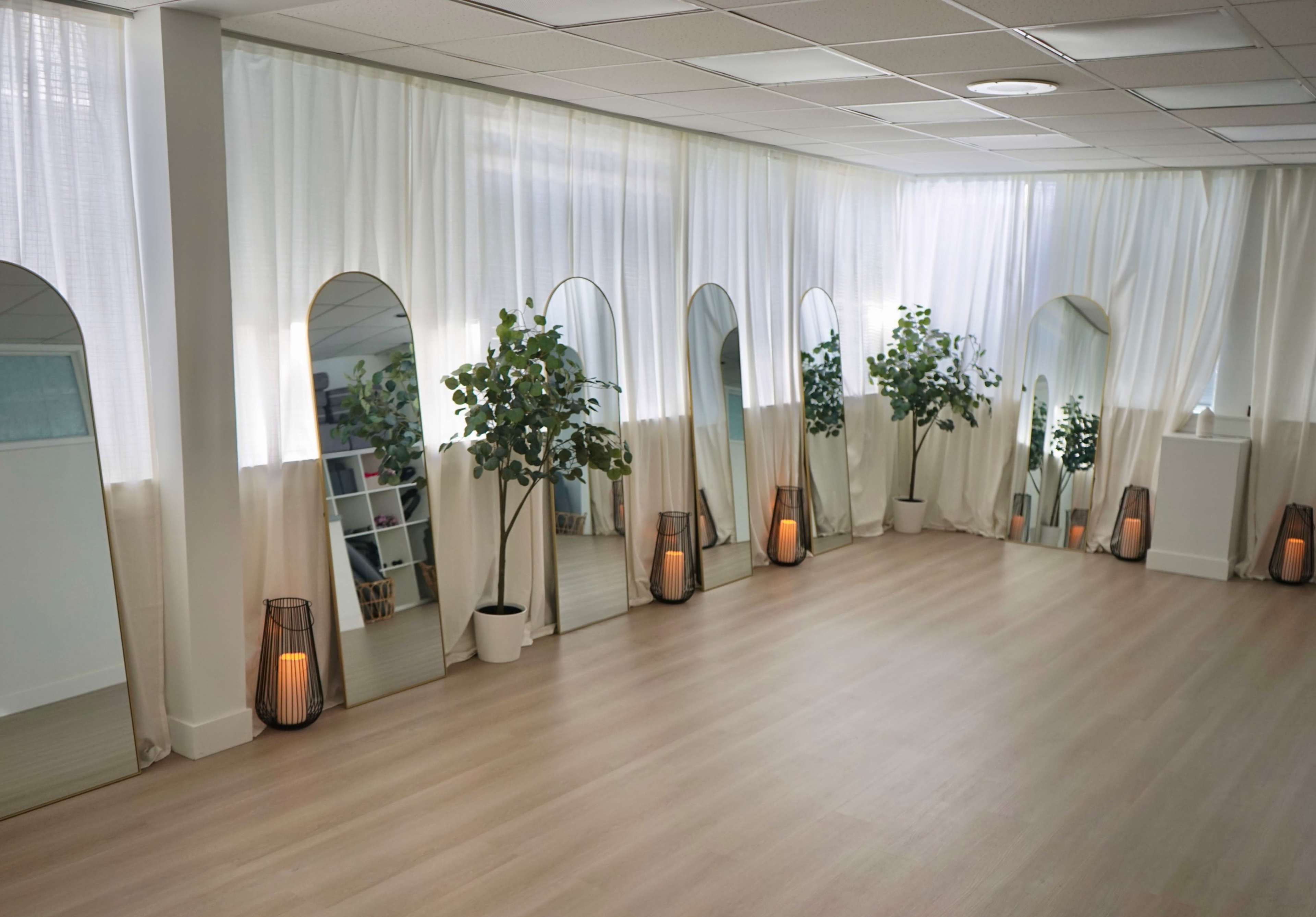 The image shows a spacious, well-lit room with multiple mirrors, potted plants, and soft lighting arranged along the walls.