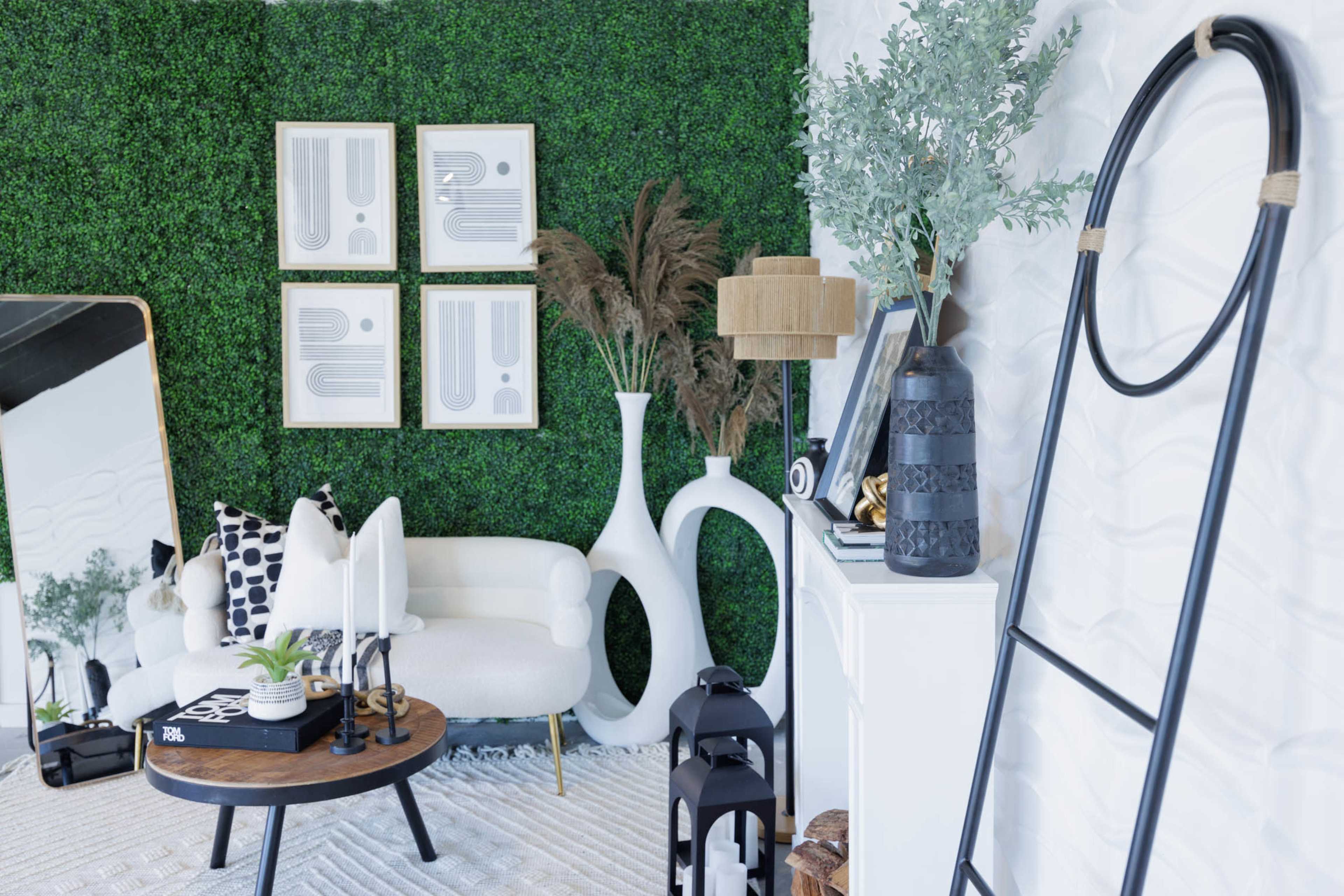 The image depicts a stylish living room scene featuring a white sofa, decorative plants, modern artwork on a green wall, and various decor items on display.