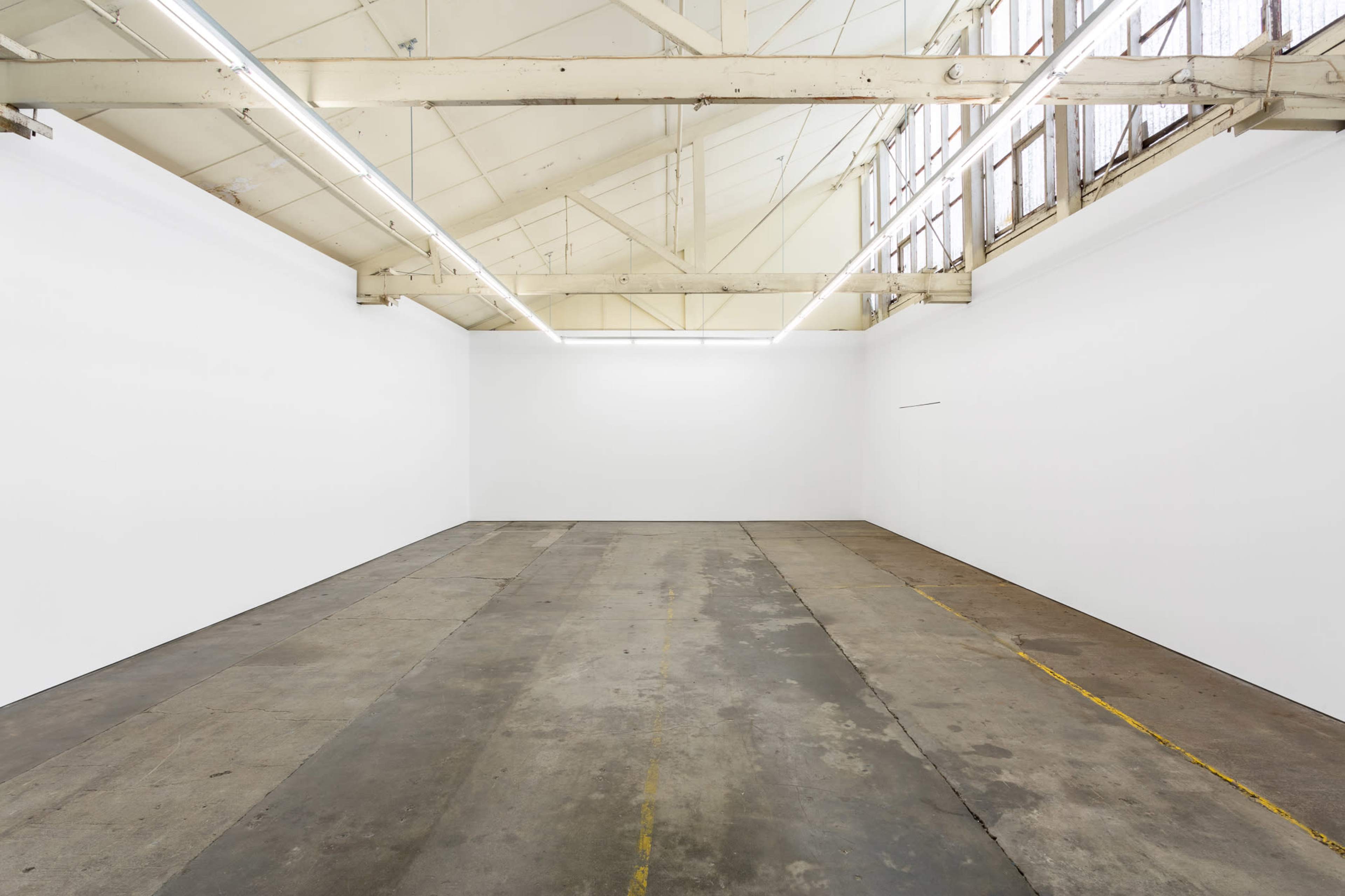 The image shows a large, empty industrial space with white walls and a concrete floor under bright overhead lights.