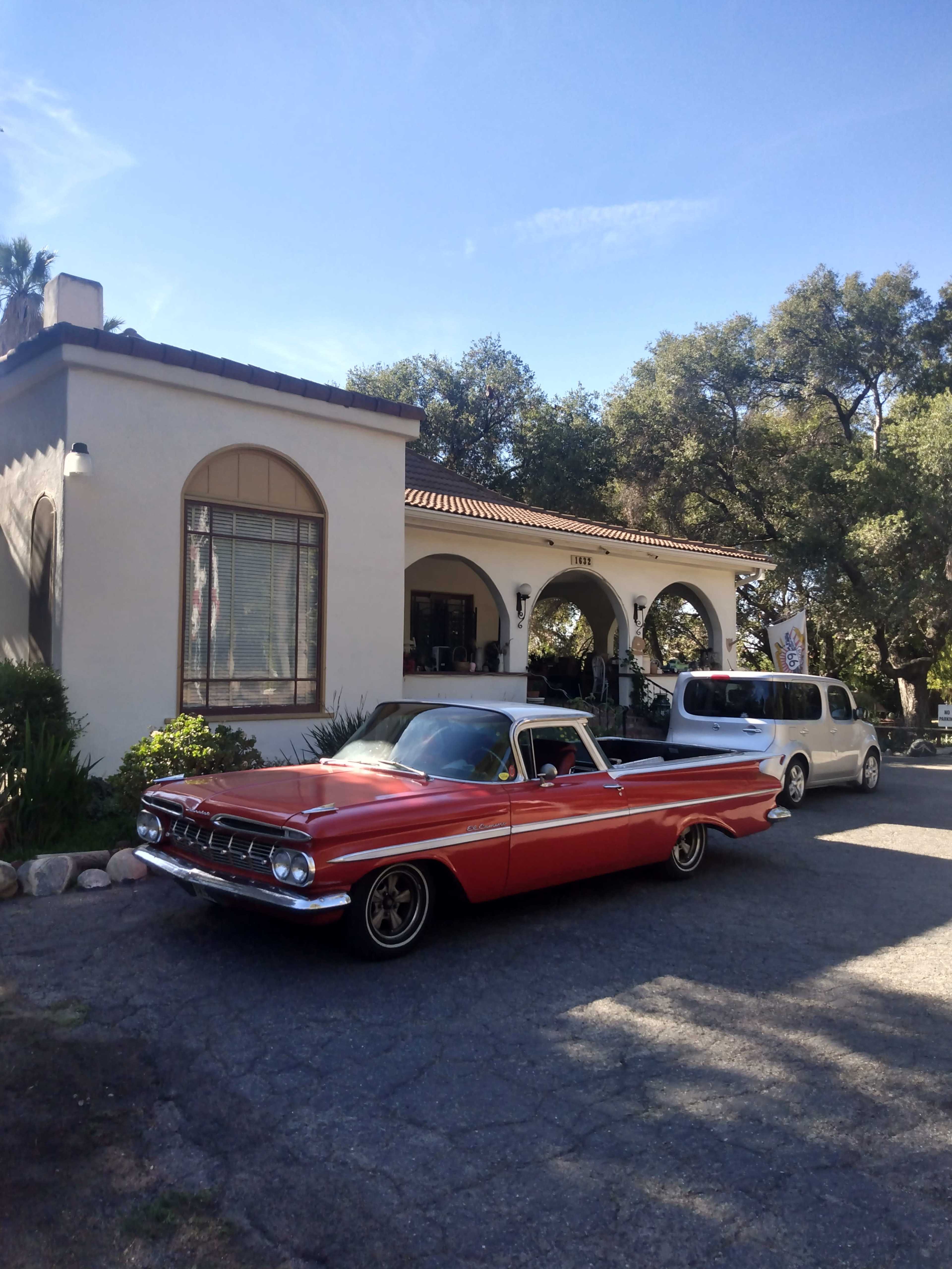 A vintage red car is parked in front of a white stucco building with arched windows and a tiled roof.