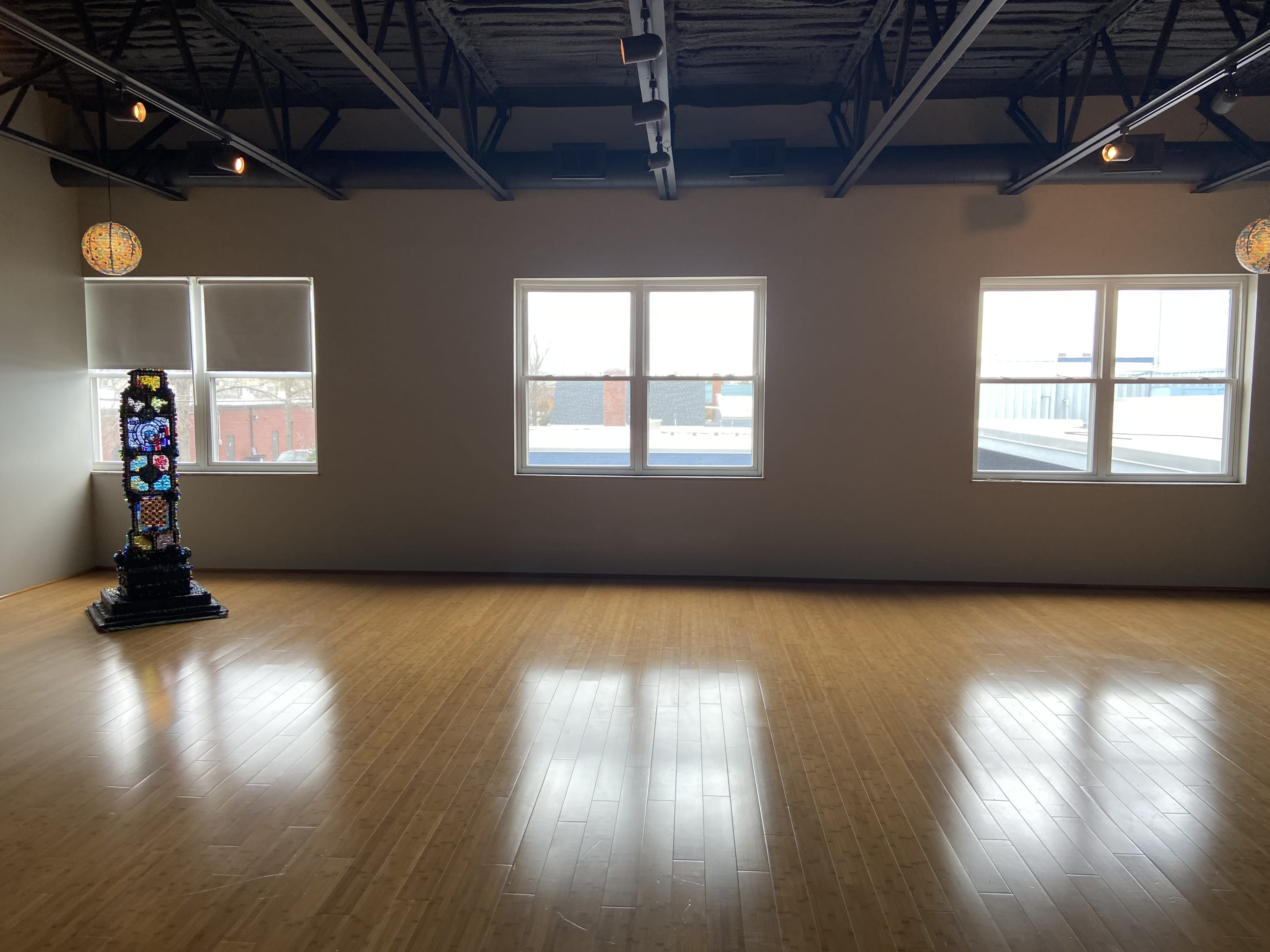 A spacious room with wooden flooring, featuring three windows and a decorative column in the corner.