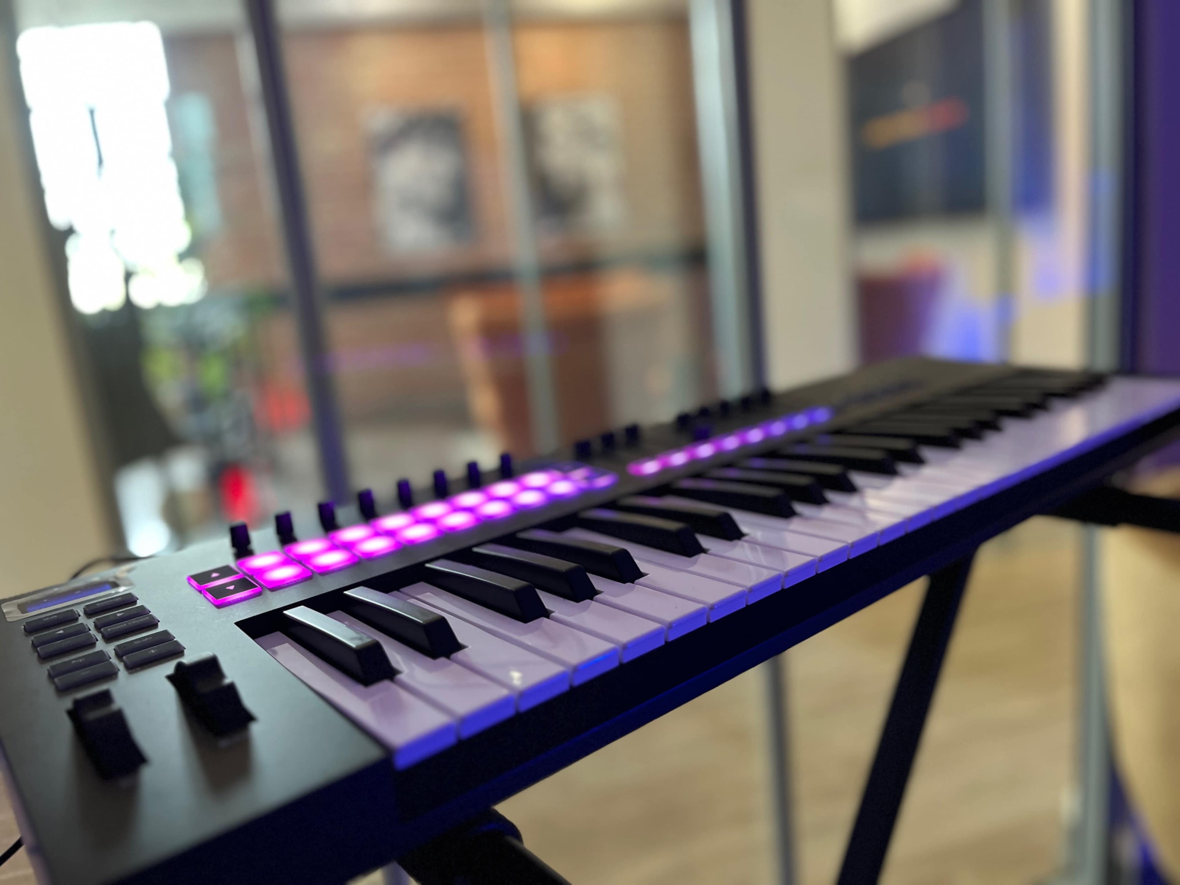 A keyboard with illuminated controls sits on a stand in a modern indoor space.