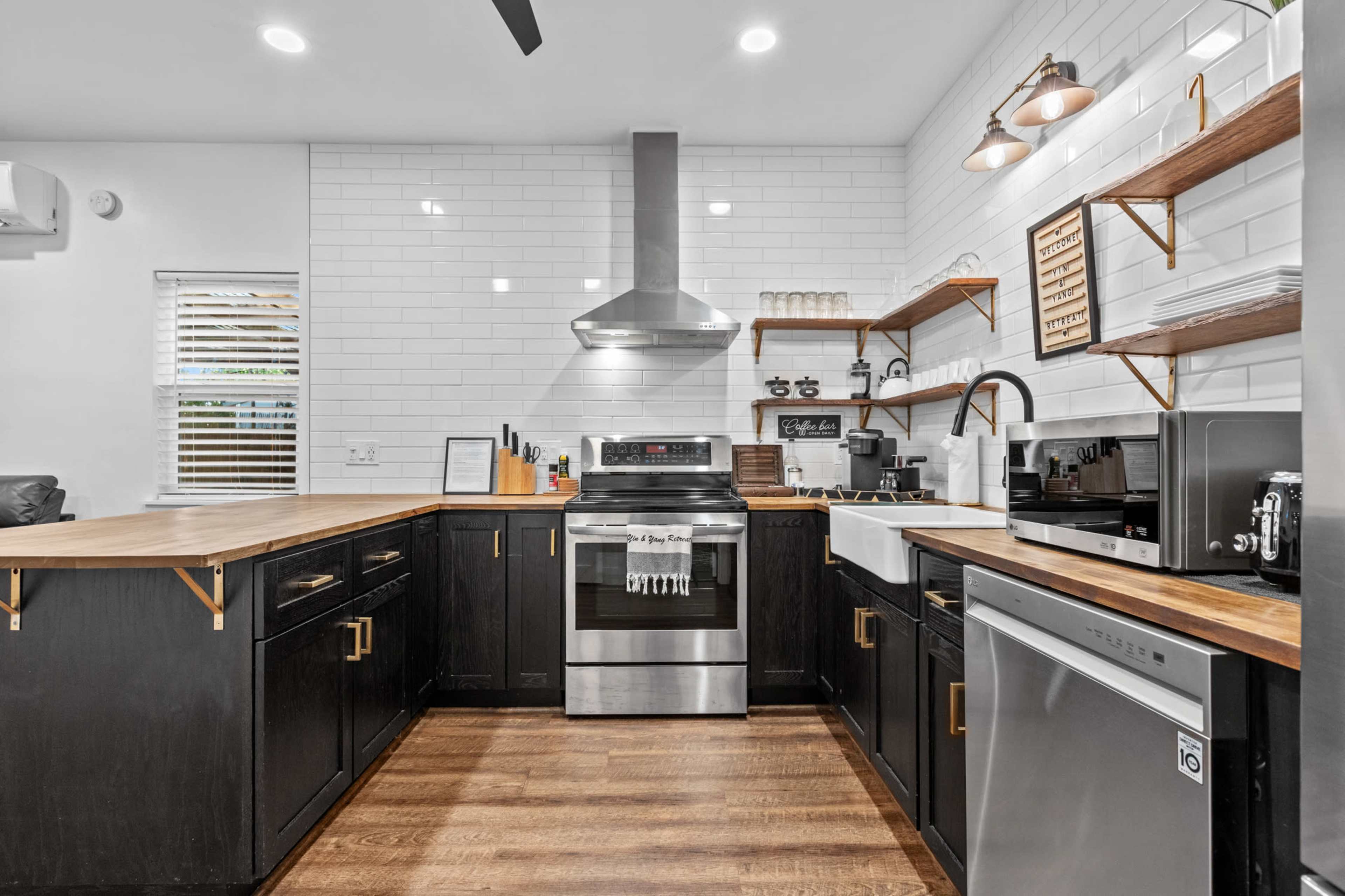 The kitchen features dark cabinetry, a stainless steel stove, and a white tiled backsplash with wooden shelves displaying kitchenware.