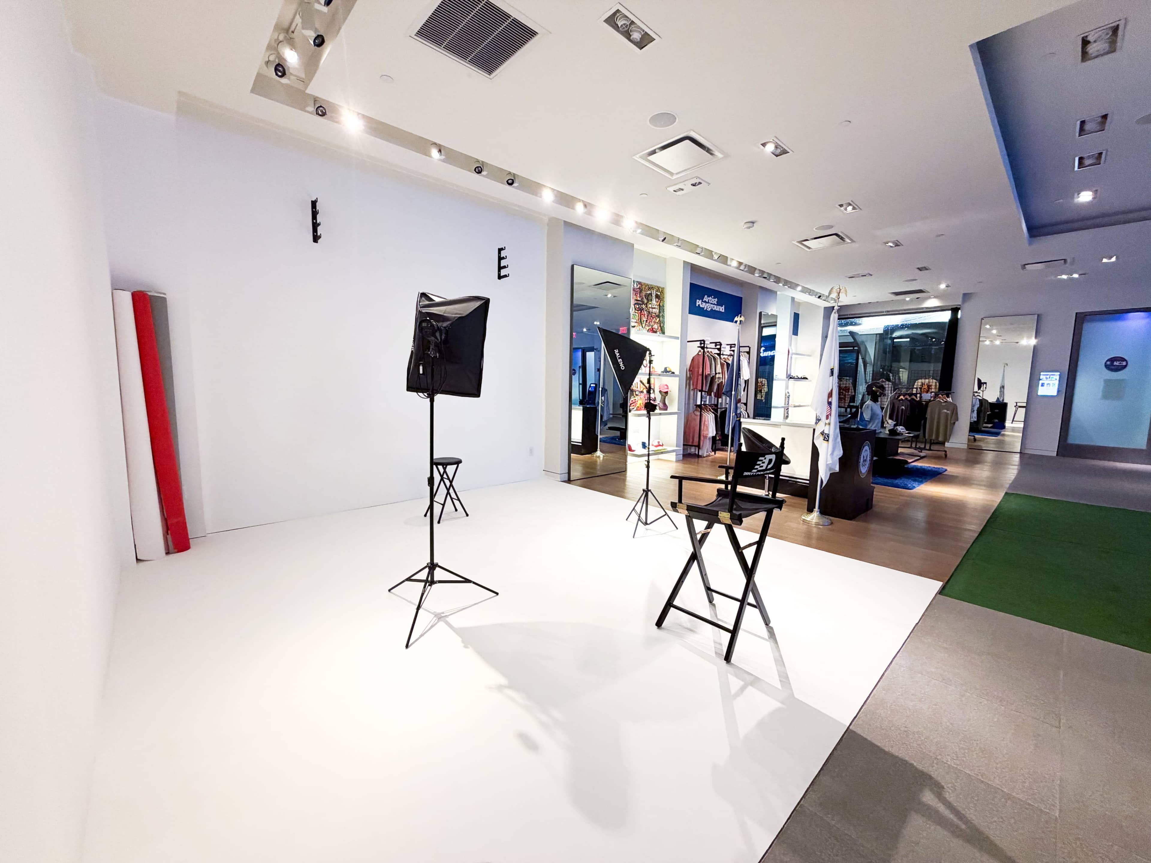 The image shows a minimalist photography studio setup with two director's chairs, studio lights, and a clear background, located within a retail space.