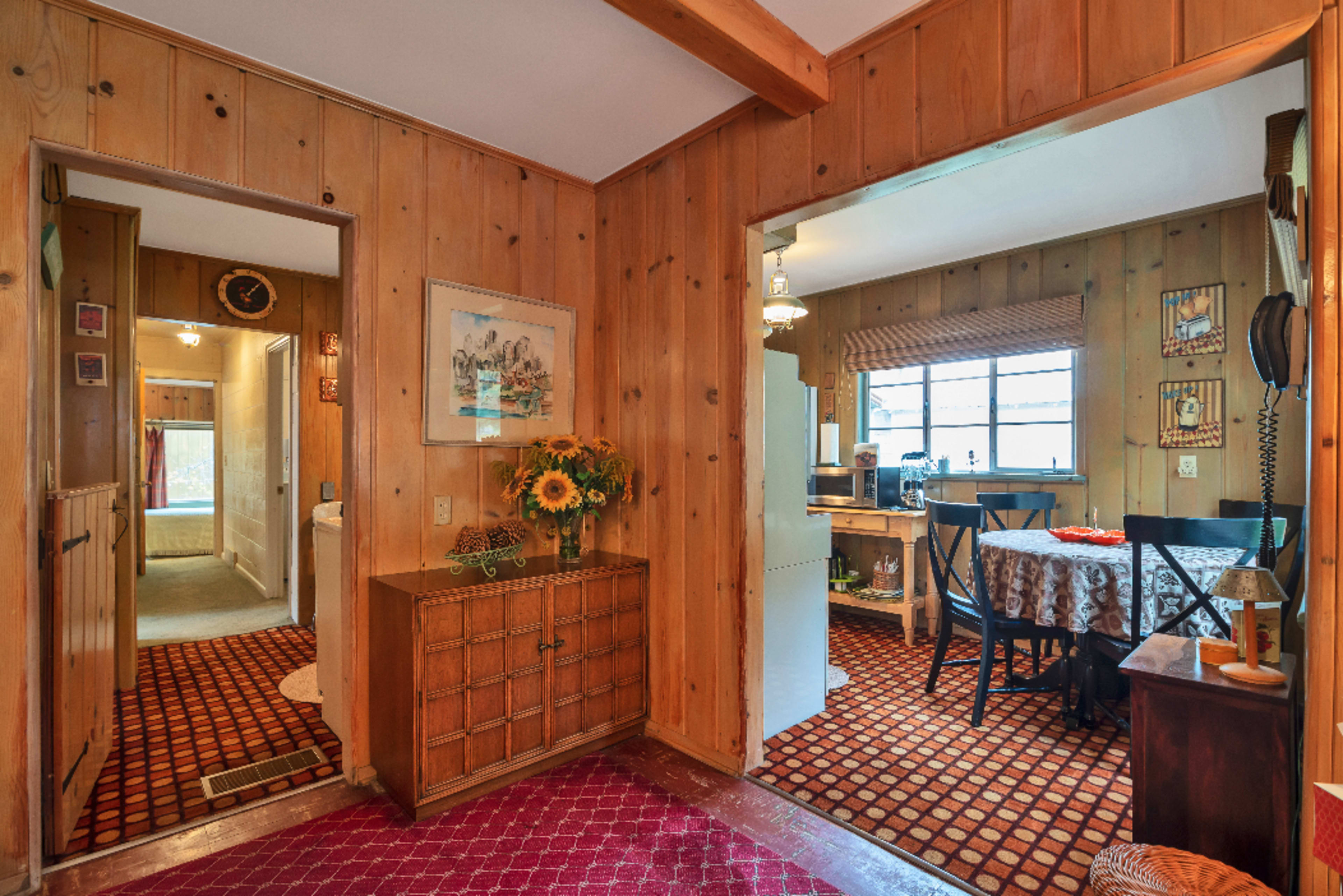 A wooden-paneled interior with a hallway leading to a bathroom on the left and a dining area with a table on the right.