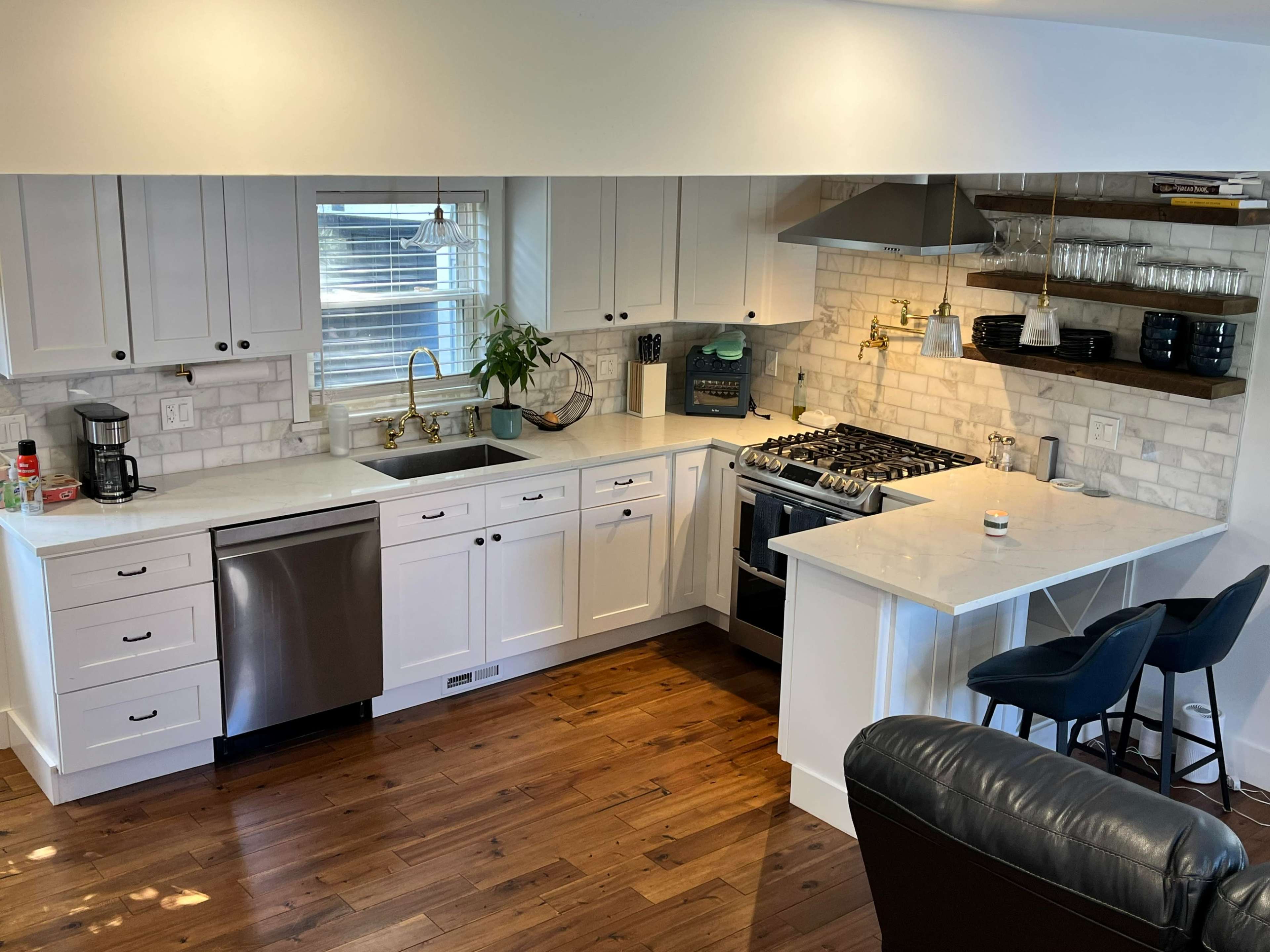 The image shows a modern kitchen featuring white cabinets, a stainless steel refrigerator, a gas stove, and a wooden countertop with bar stools.