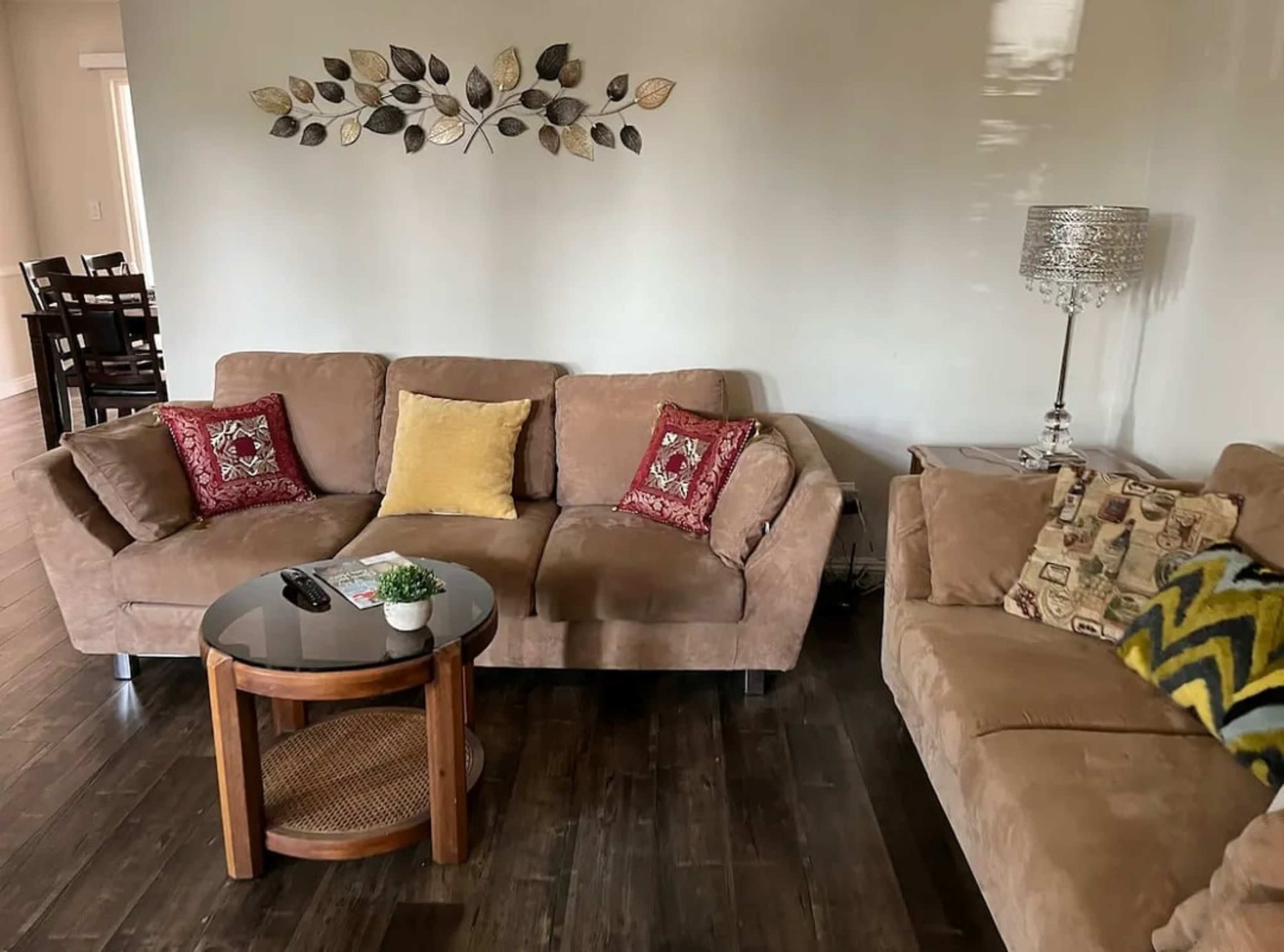 The image shows a living room with two brown sofas, a round wooden coffee table, and decorative leaves on the wall.