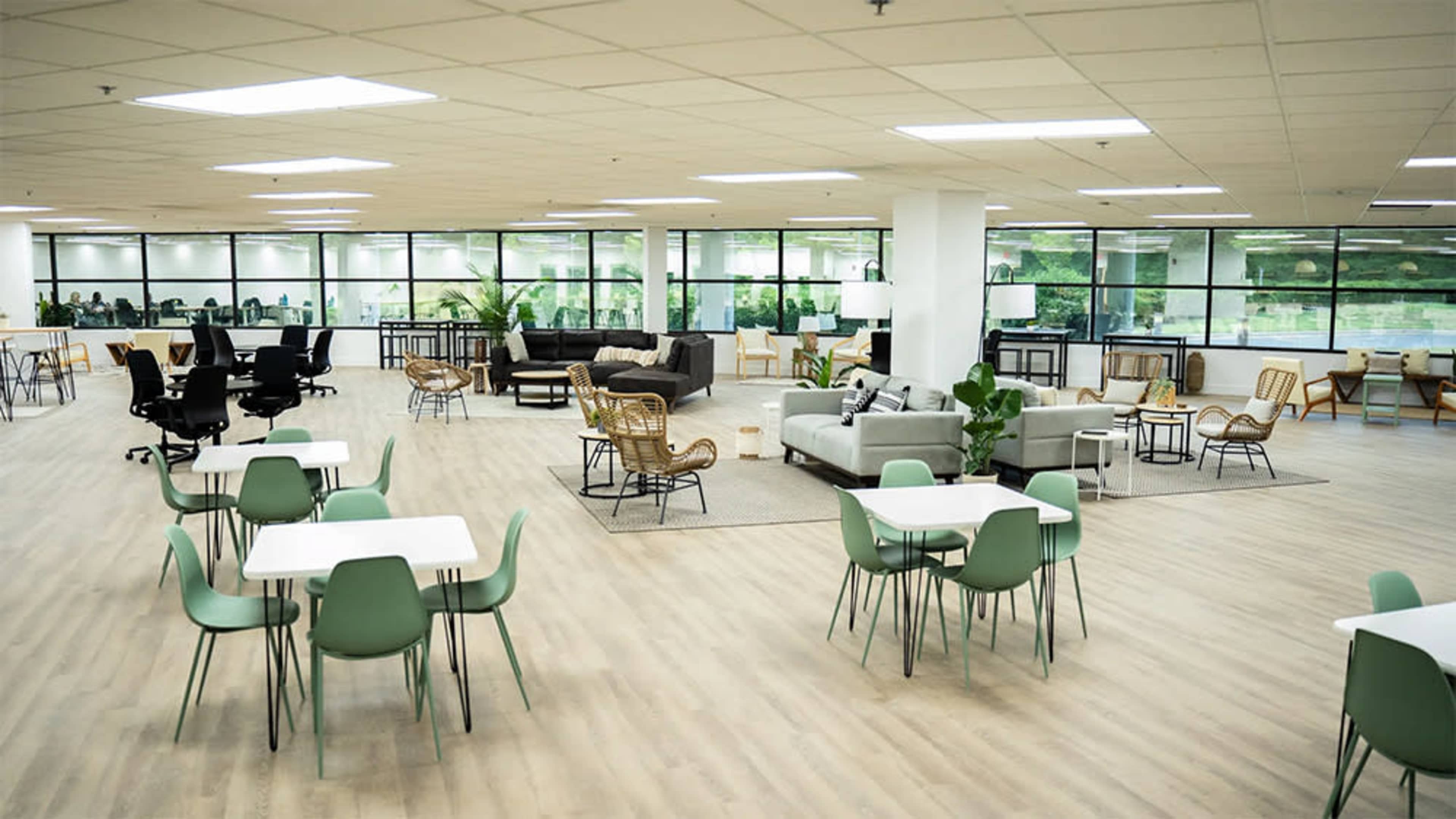 A spacious office area with various seating arrangements, including tables and chairs, sofas, and plants.