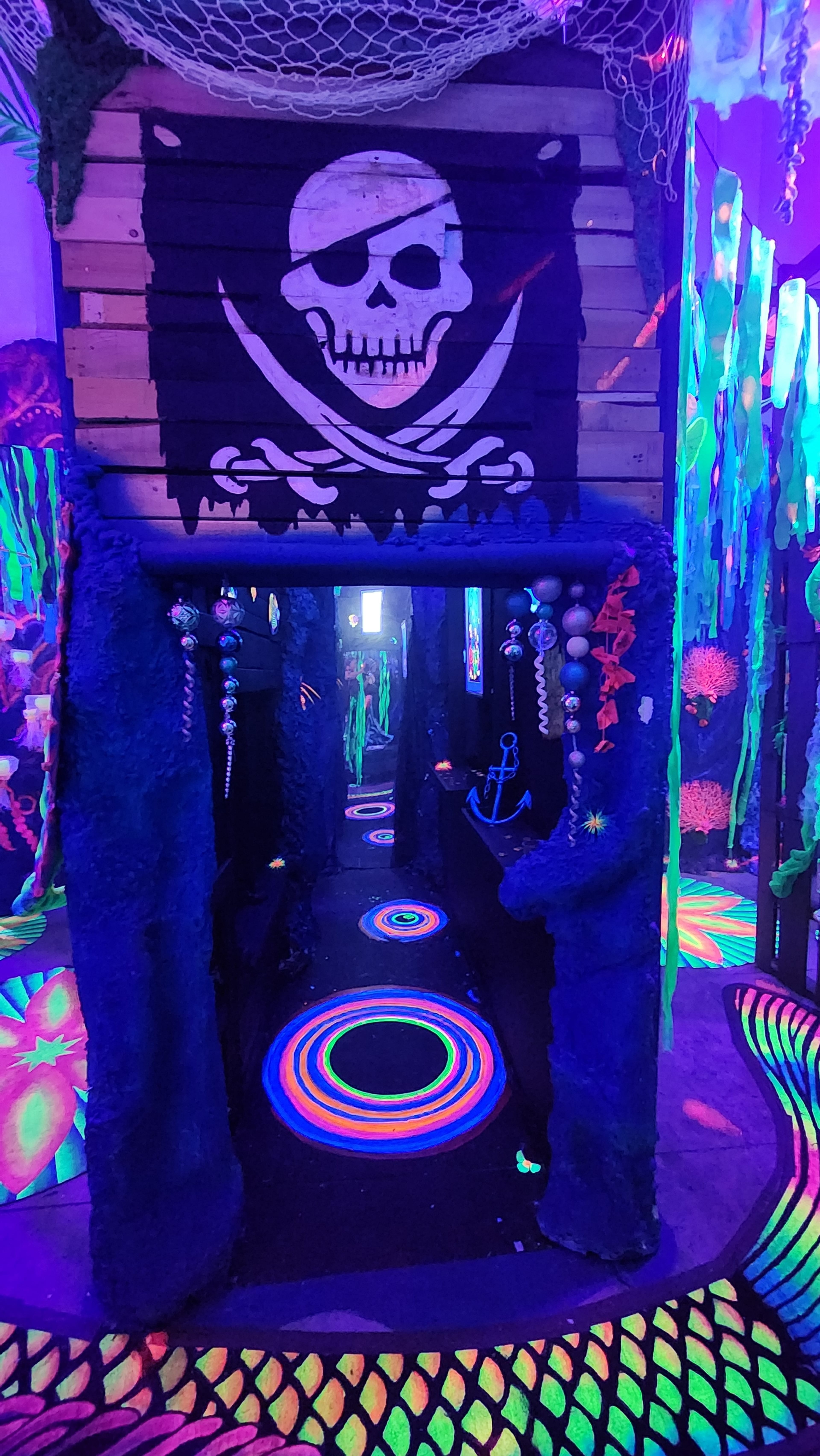 A brightly colored, glow-in-the-dark tunnel decorated with pirate-themed art, including a skull and crossbones banner.