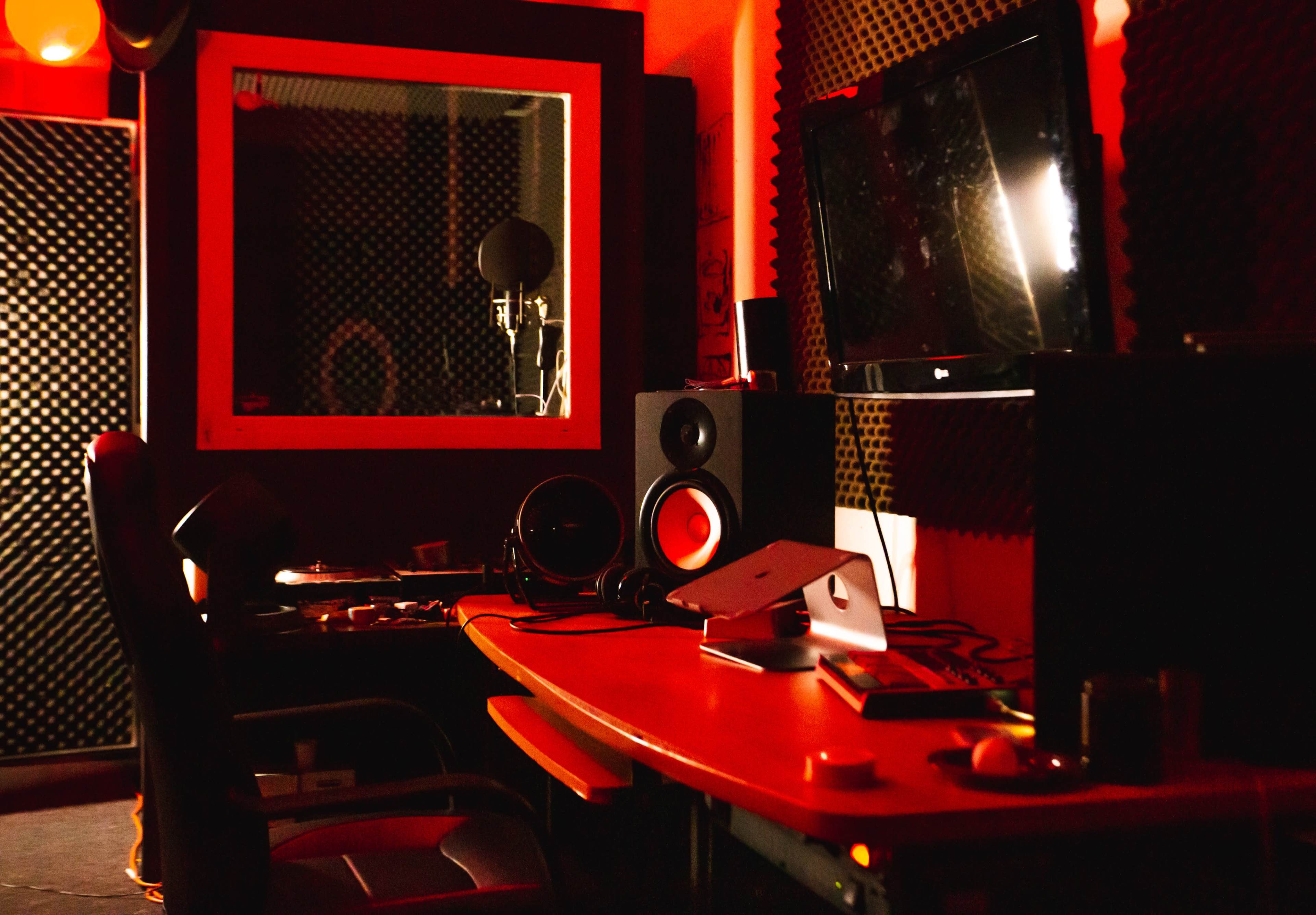 A recording studio equipped with soundproof panels, a microphone, a television, and a desk with audio equipment.