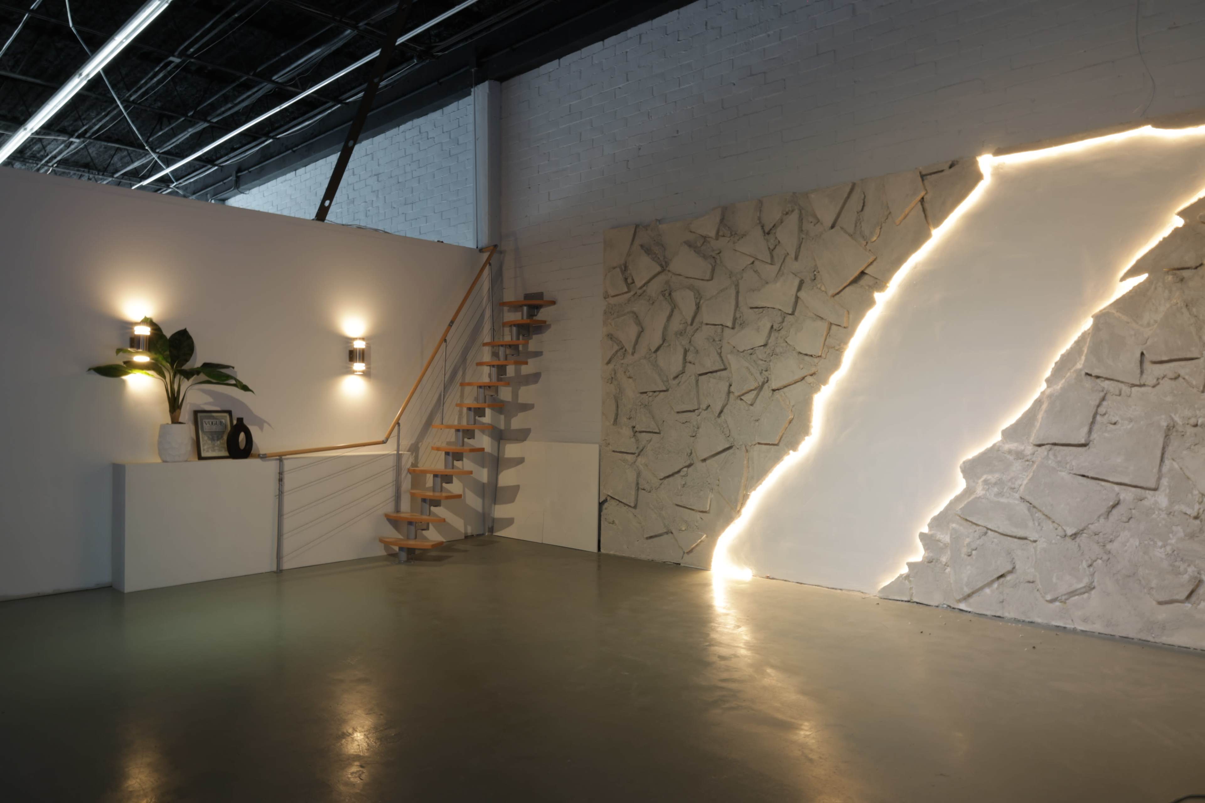 The image shows a modern interior space featuring a staircase, a decorative wall with a lighted crack, and minimalist lighting fixtures.