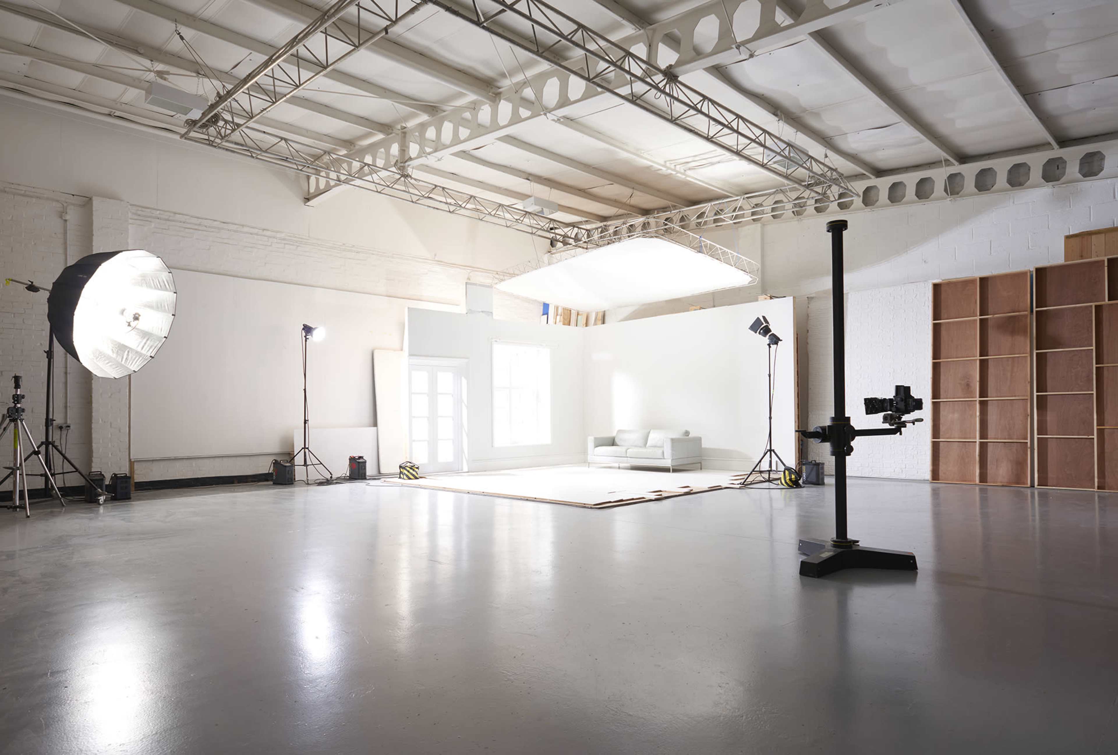 A large photography studio with a white backdrop, lighting equipment, and a simple sofa placed in the center.