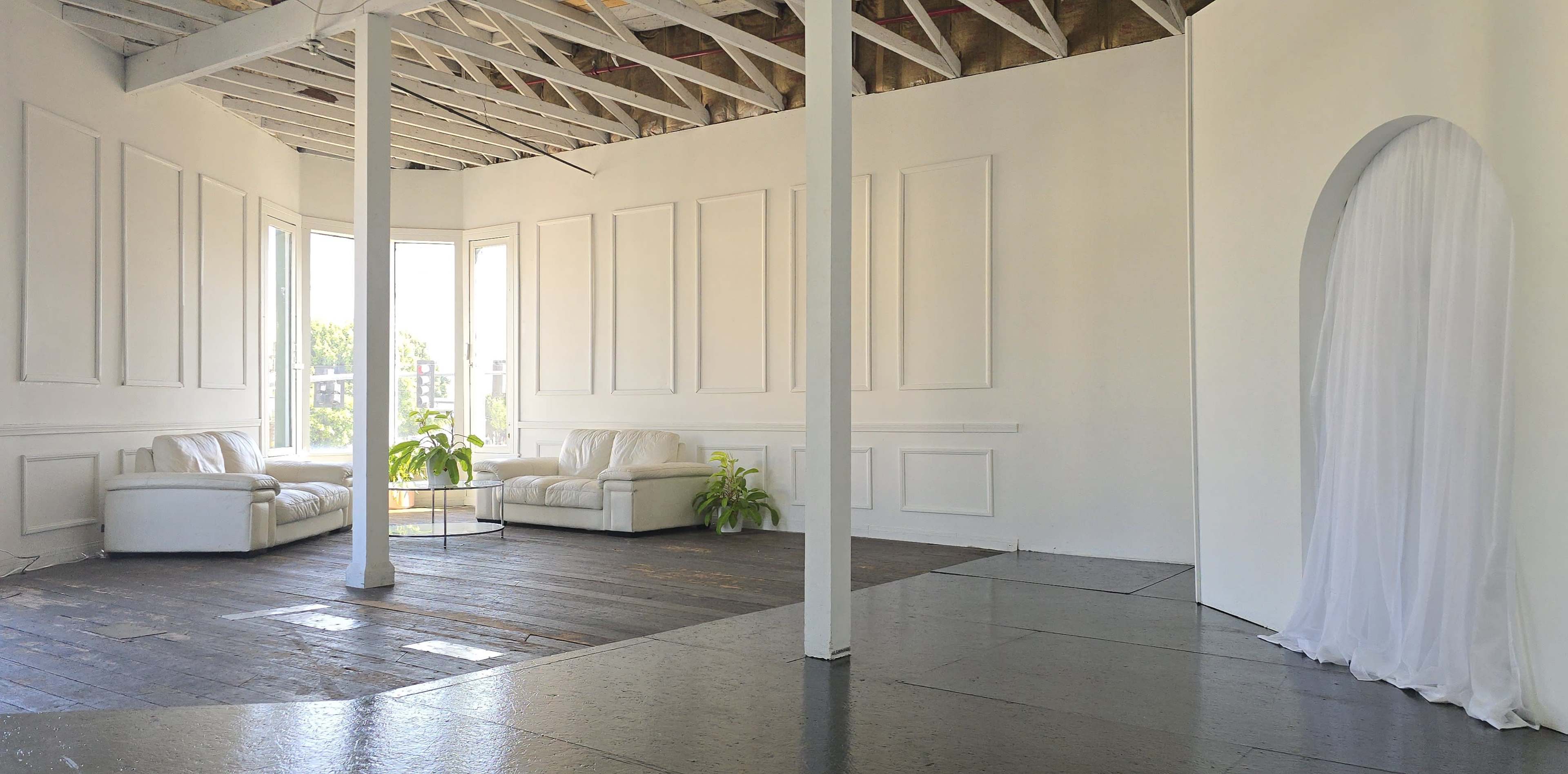 A spacious, white interior with two white sofas, a glass table, and a large archway draped with white fabric.