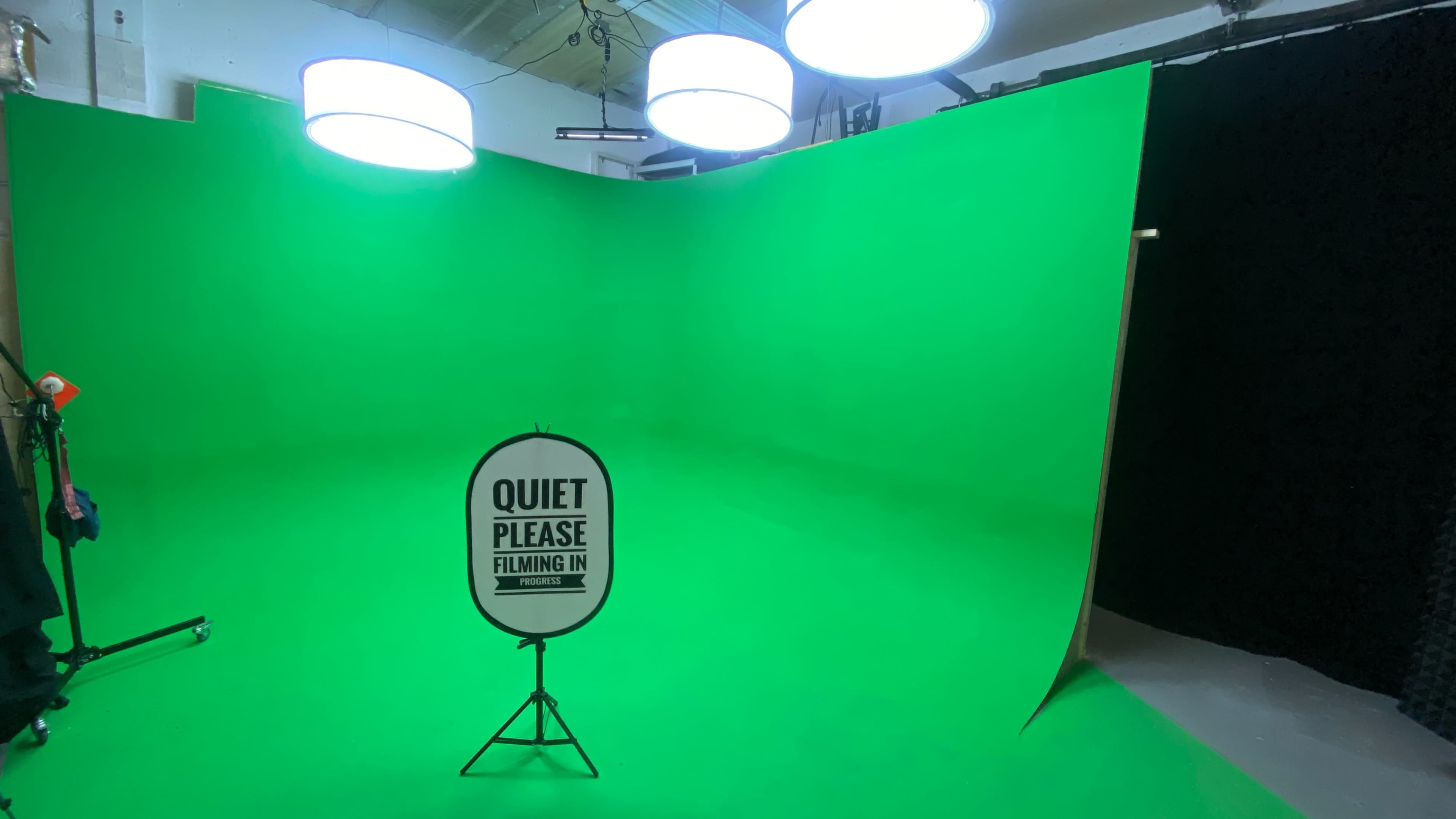 A green screen studio setup with bright lights and a sign that reads "QUIET PLEASE FILMING IN PROGRESS."