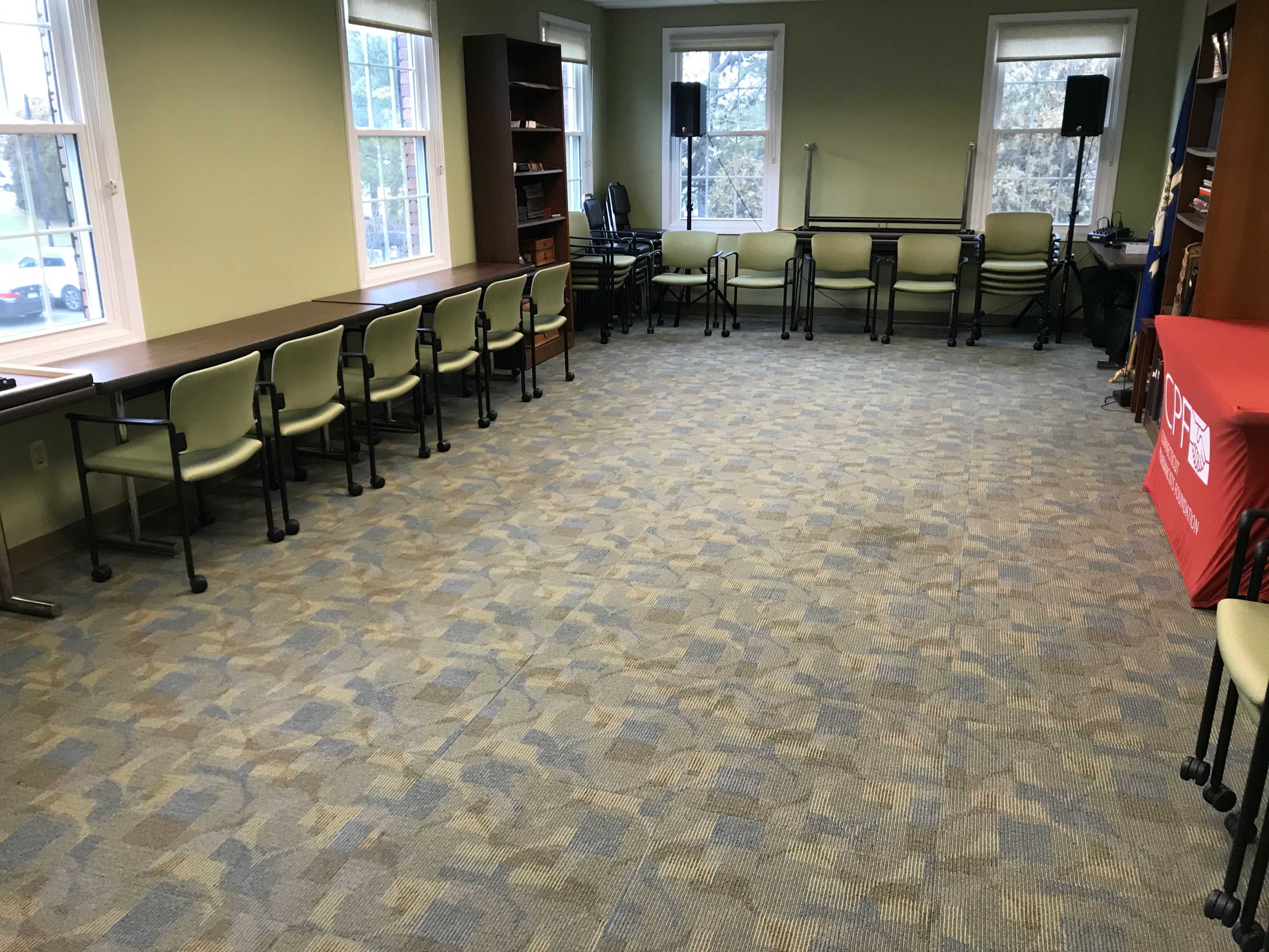 A spacious room with several chairs arranged in a semi-circle along the walls and a long table along one side.