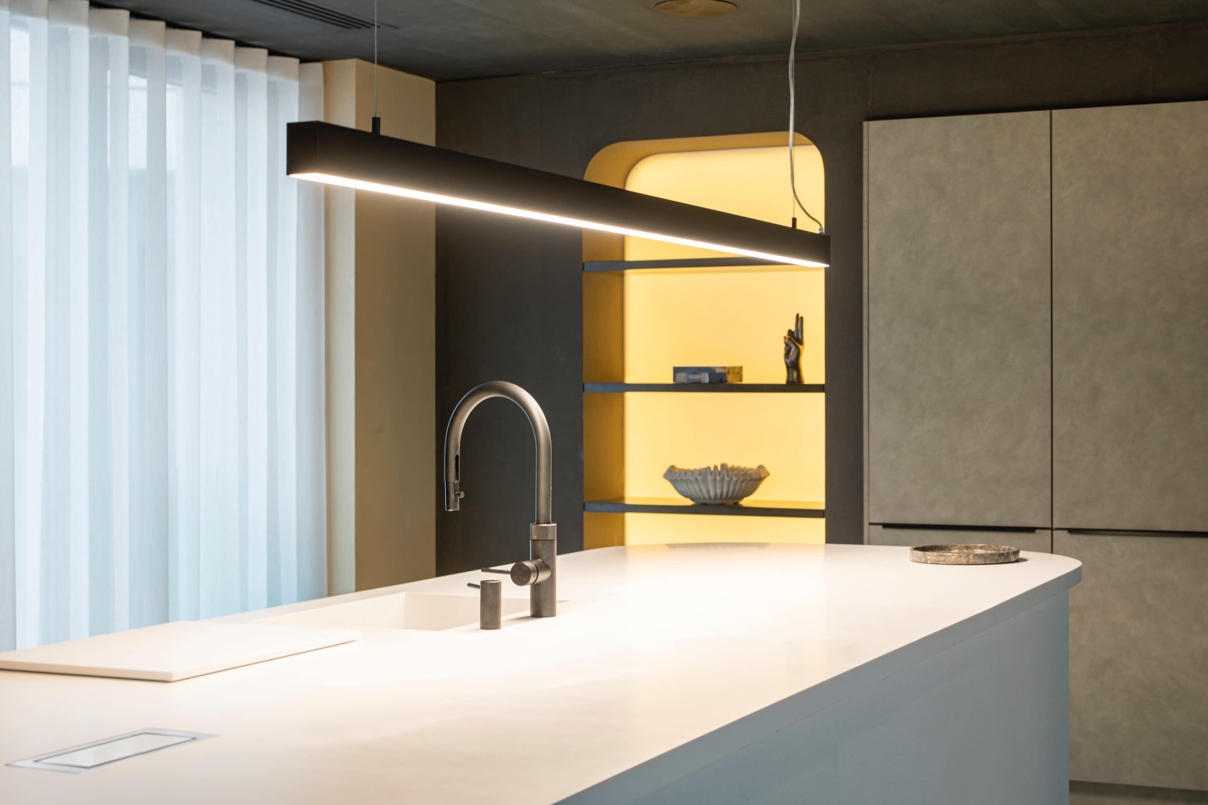 A modern kitchen features a sleek island with a minimalist faucet and a long overhead light, complemented by yellow and gray shelving.