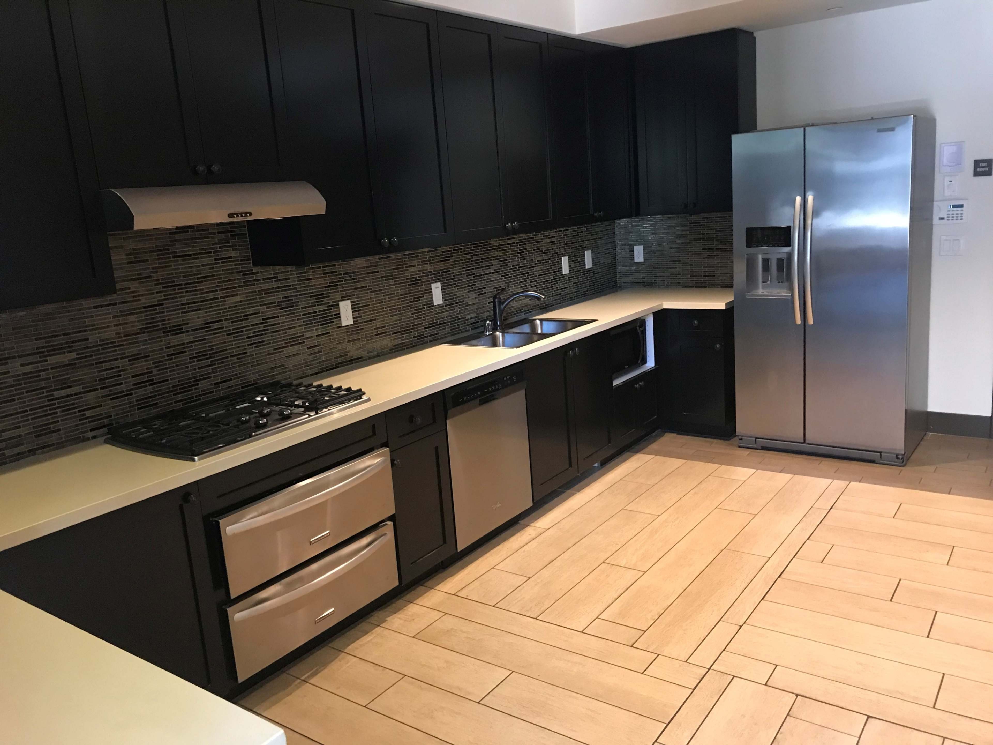 A modern kitchen with dark cabinetry, stainless steel appliances, and a tiled backsplash.