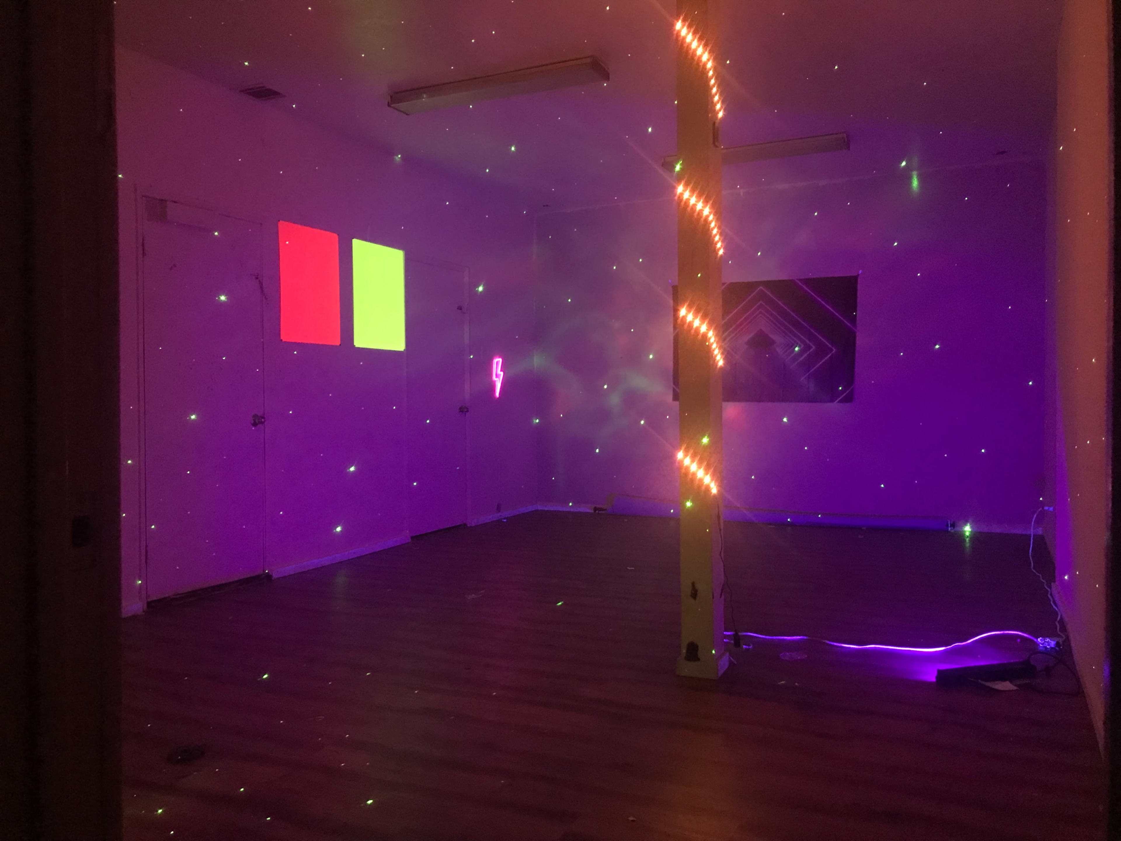An empty room with purple lighting, a column adorned with string lights, and two projected squares on the wall.
