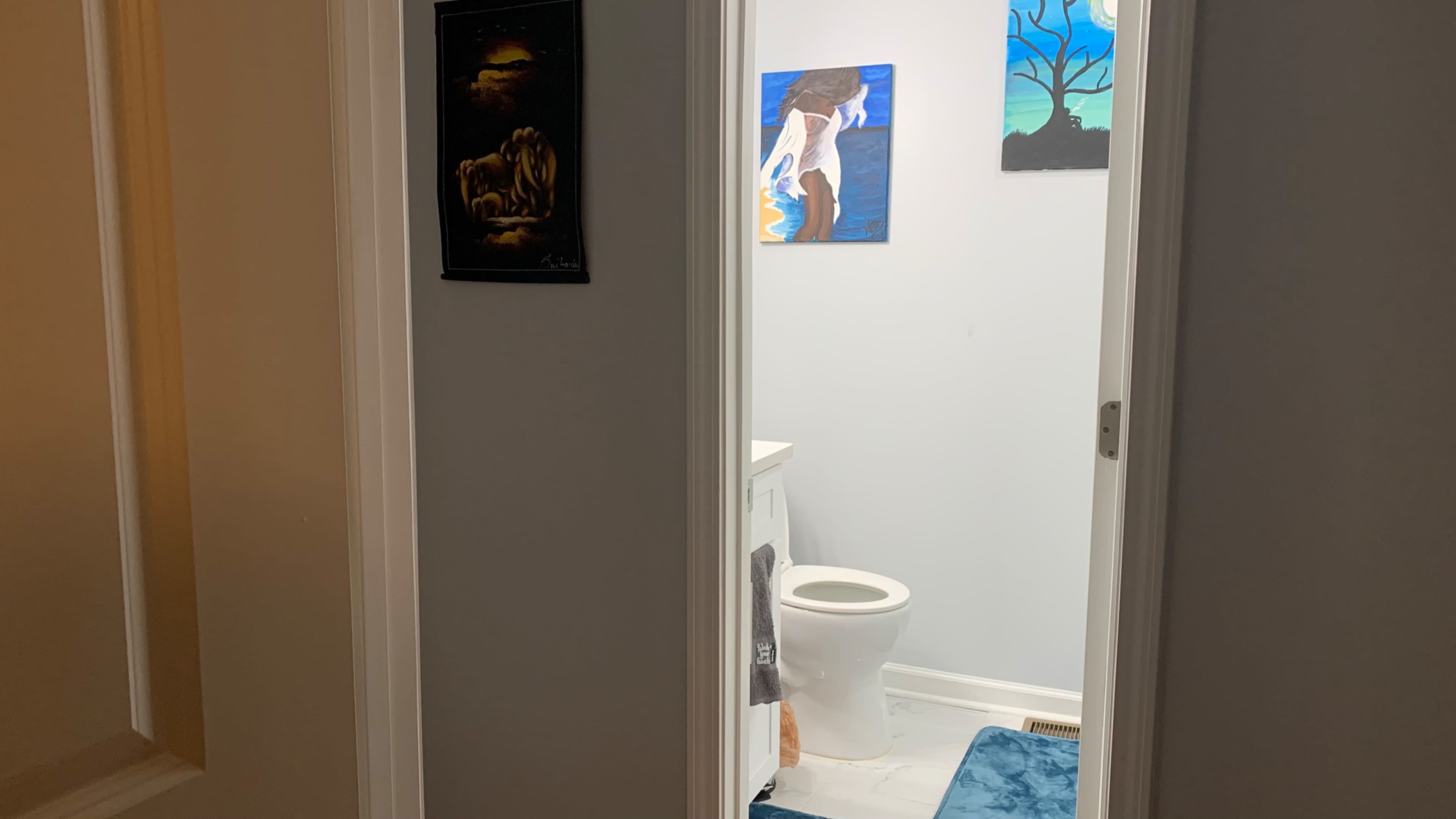 A bathroom is visible through an open door, featuring a toilet, a blue rug, and colorful artwork on the walls.