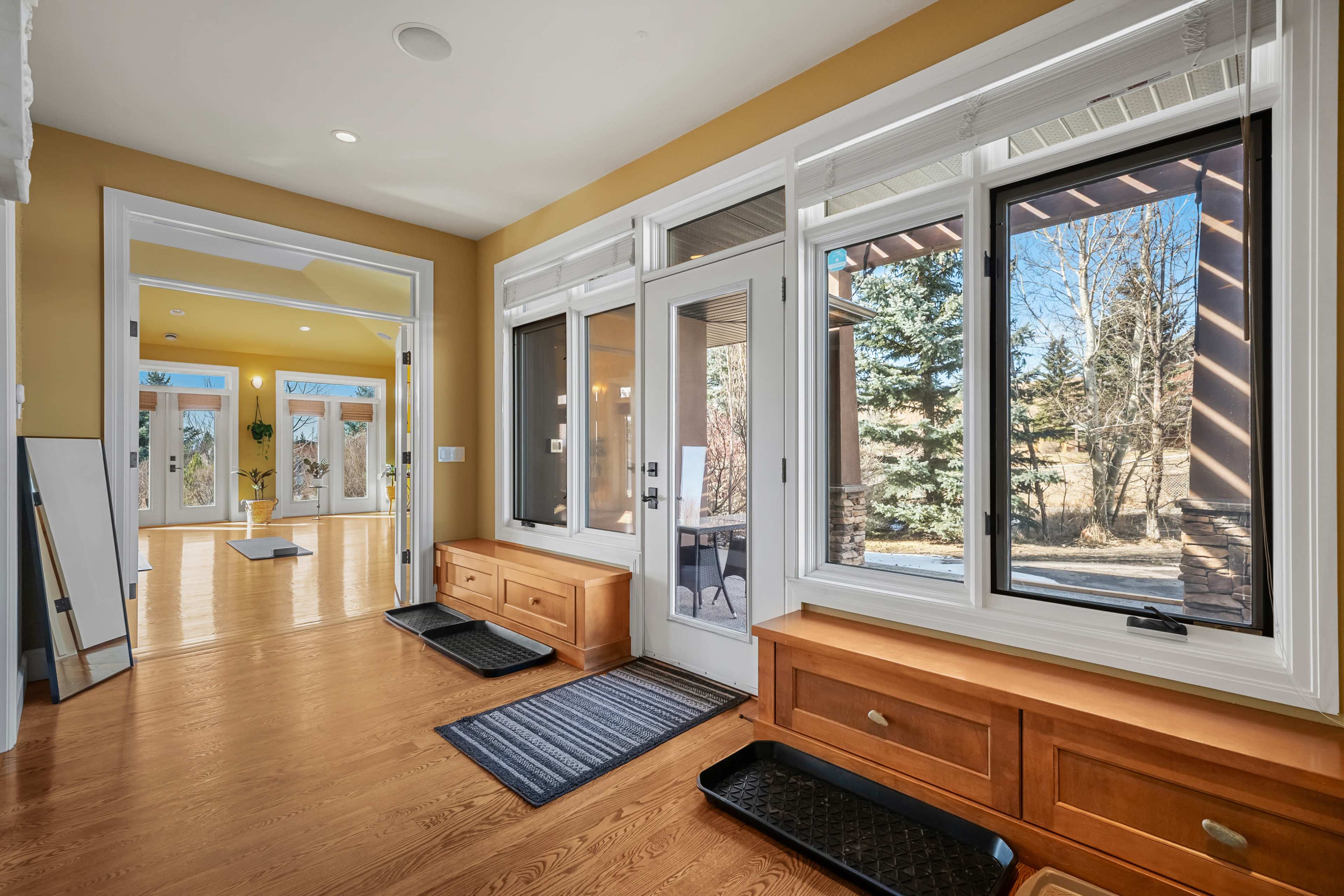 The image shows a bright entryway featuring wooden benches, large windows, and a view of trees outside.