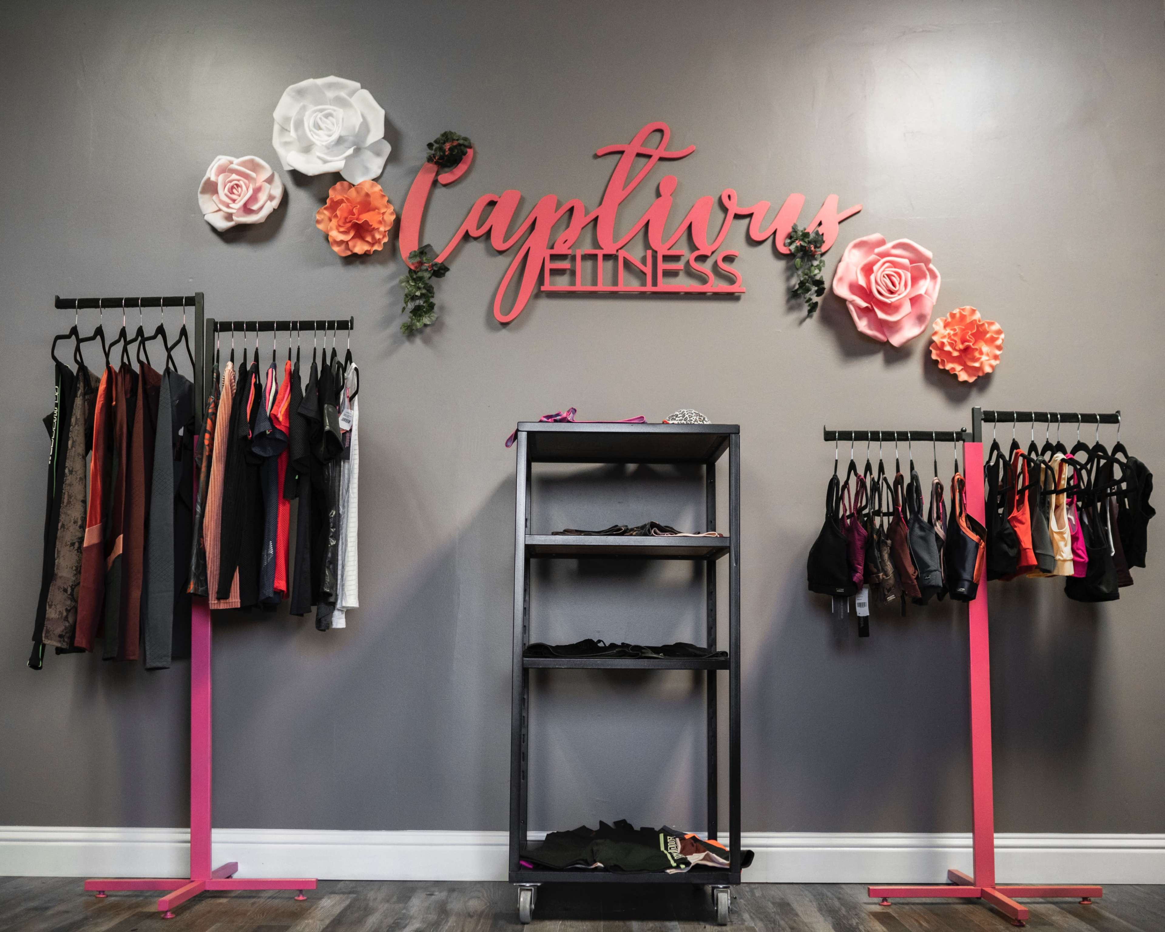 A fitness apparel store with racks of clothing on either side and a decorative sign reading "Captivus Fitness" above, accompanied by large paper flowers.