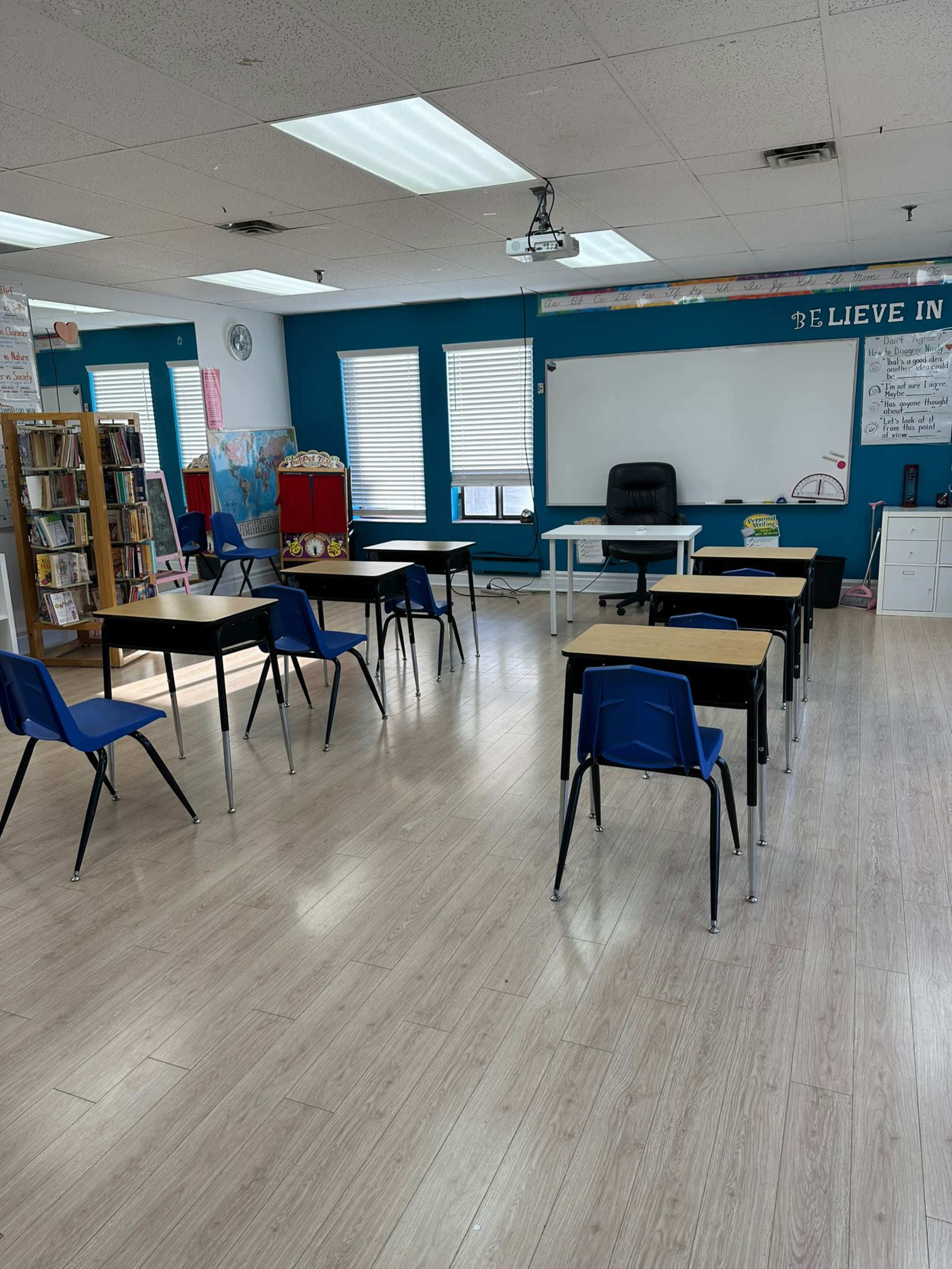 A bright classroom with several desks arranged in a rectangular layout and a large whiteboard at the front.