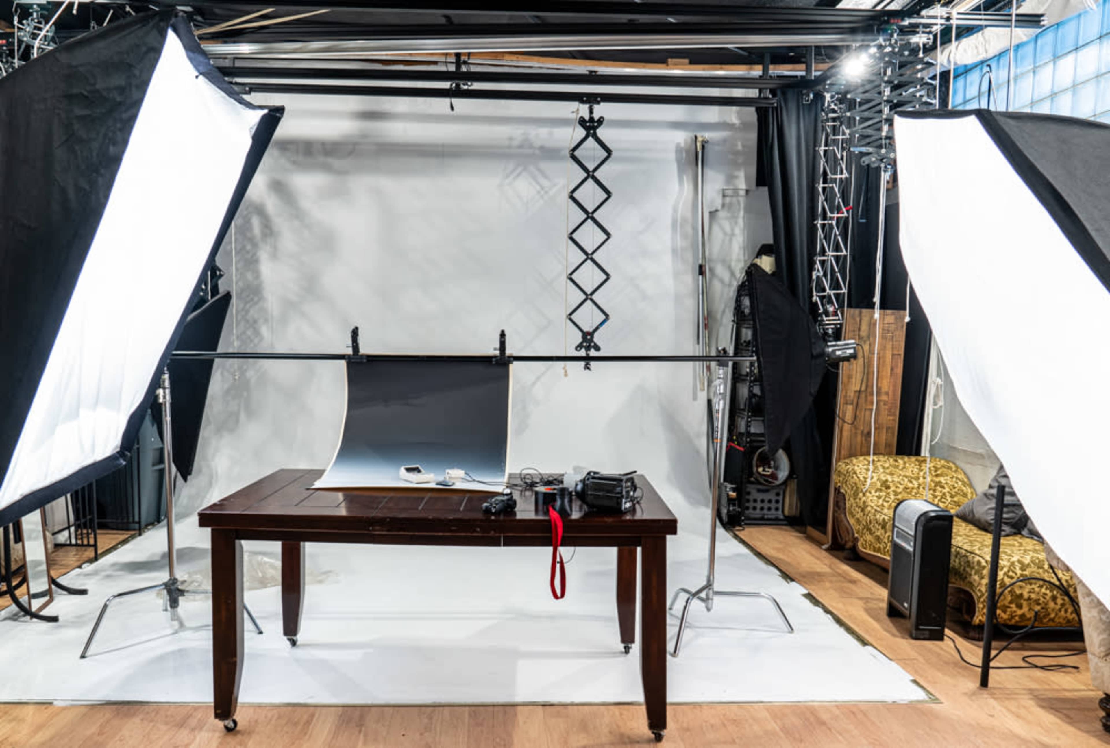 The image shows a photography studio equipped with a wooden table, lighting equipment, and a backdrop set up for a photo shoot.