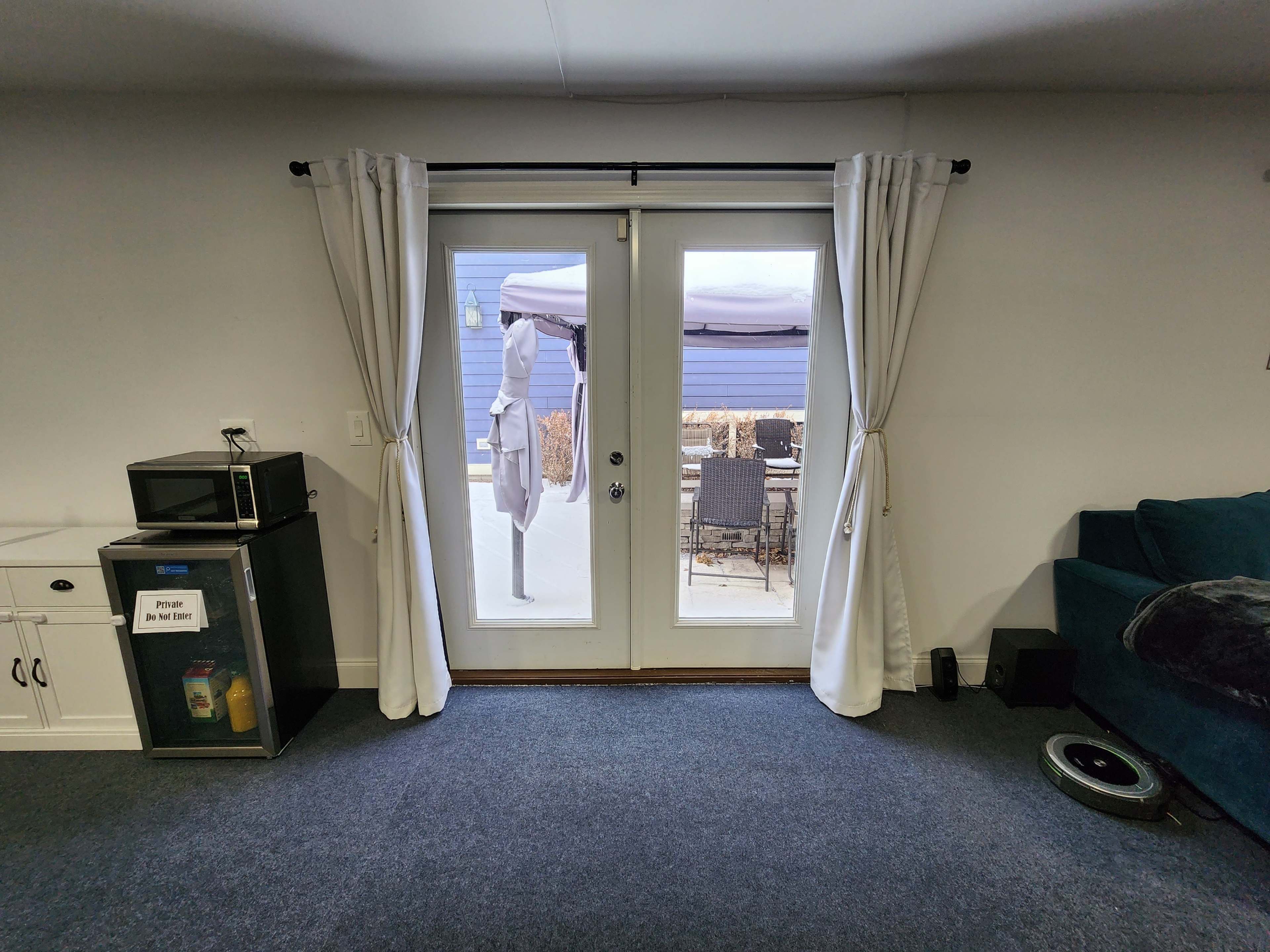 A living area with a blue couch, a microwave on a side cabinet, and two glass doors leading to an outdoor patio.