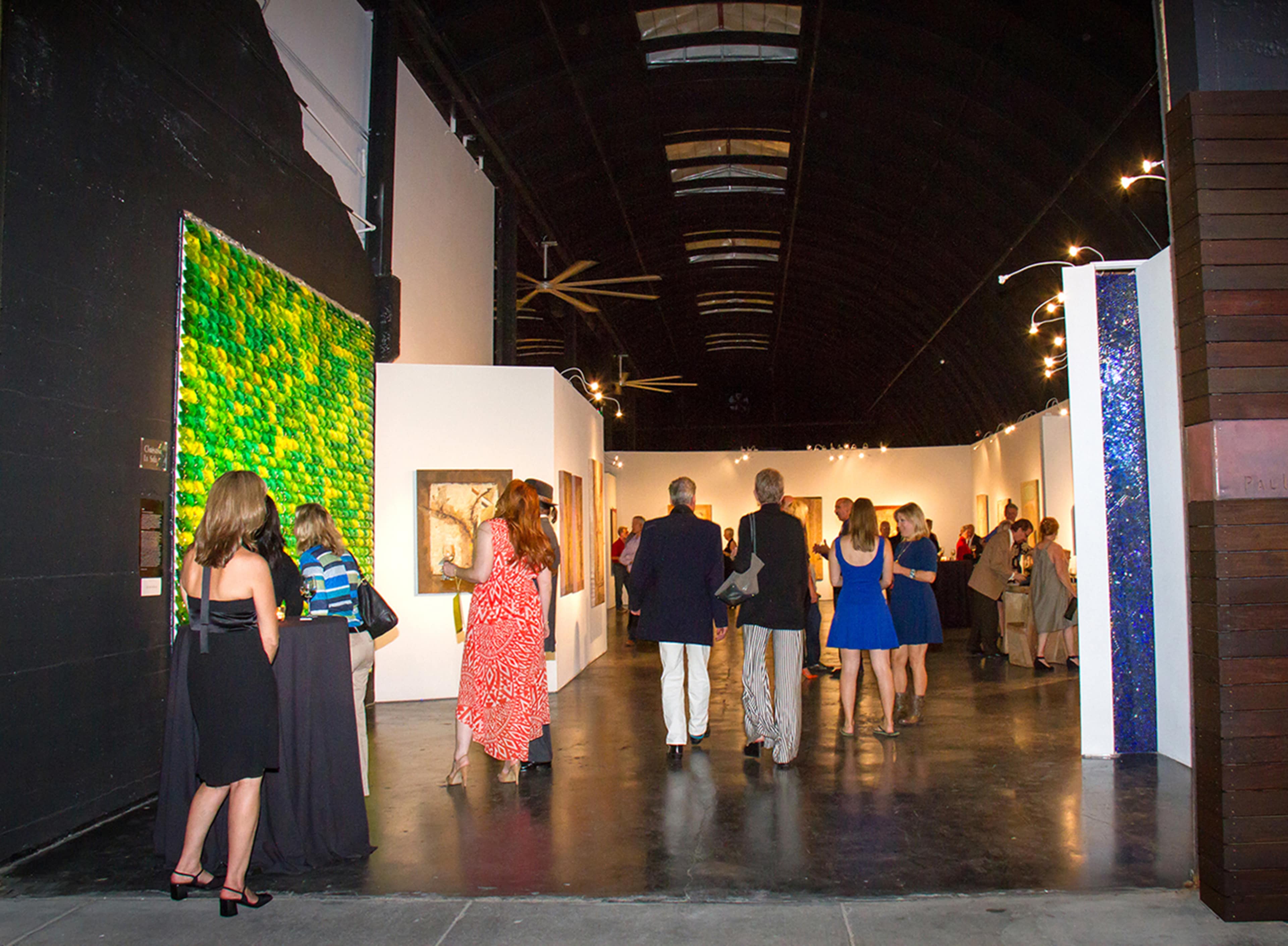 A group of people browse an art gallery featuring colorful paintings along the walls.