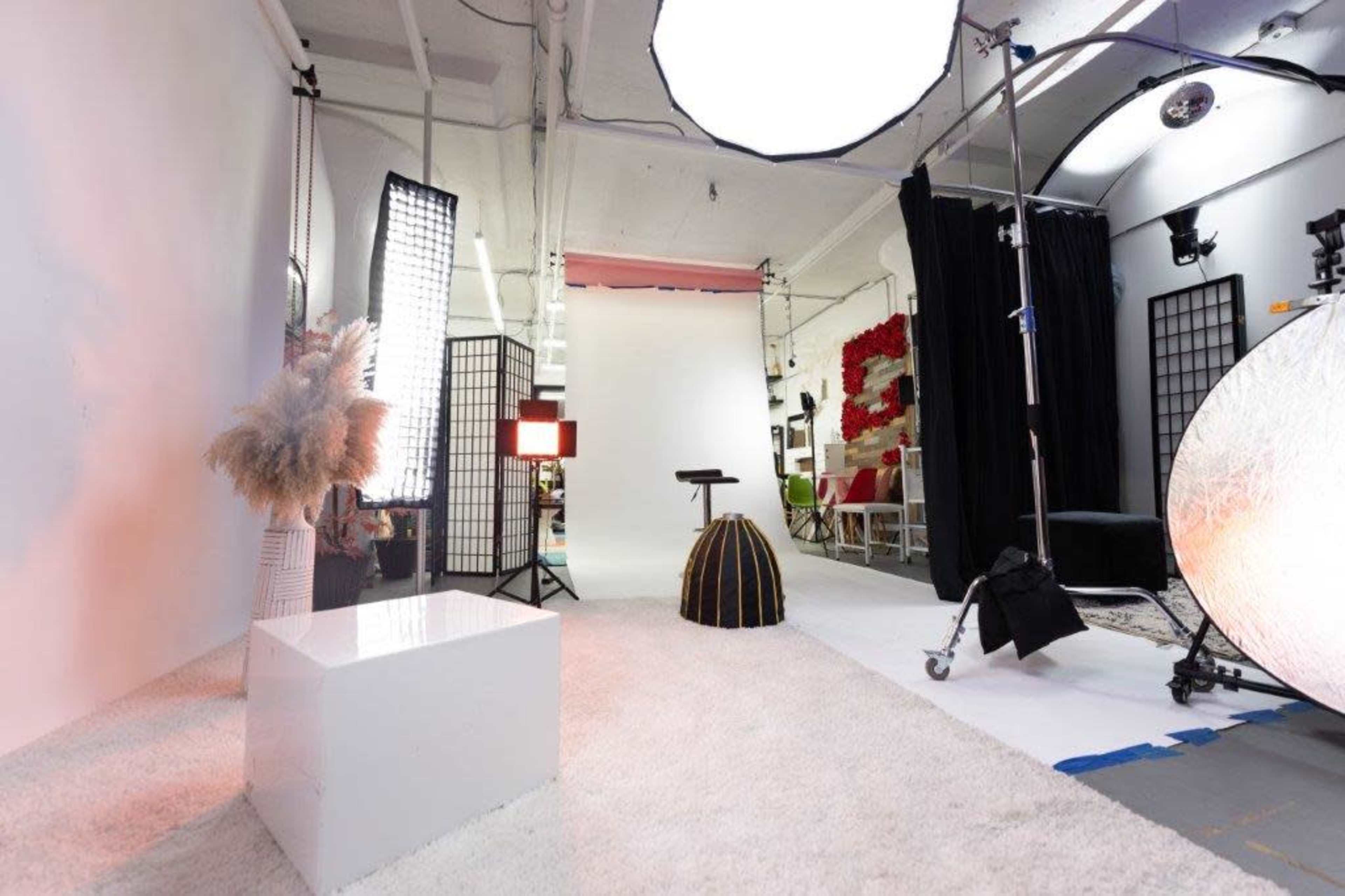 The image shows a photography studio setup with various light sources, backdrops, and props arranged on a carpeted floor.
