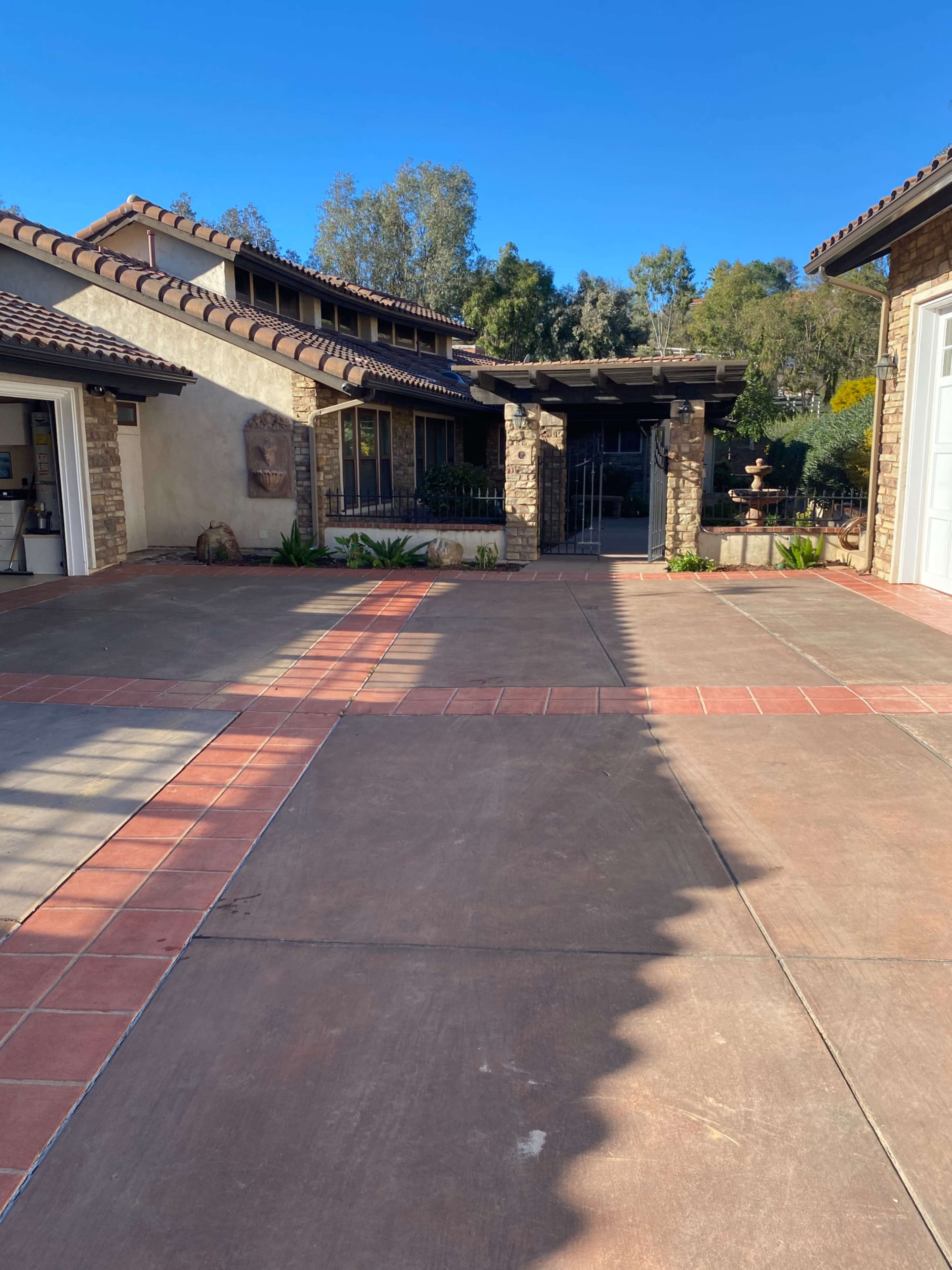 The image shows a driveway leading to a house with stone and stucco architecture, surrounded by trees and landscaping.