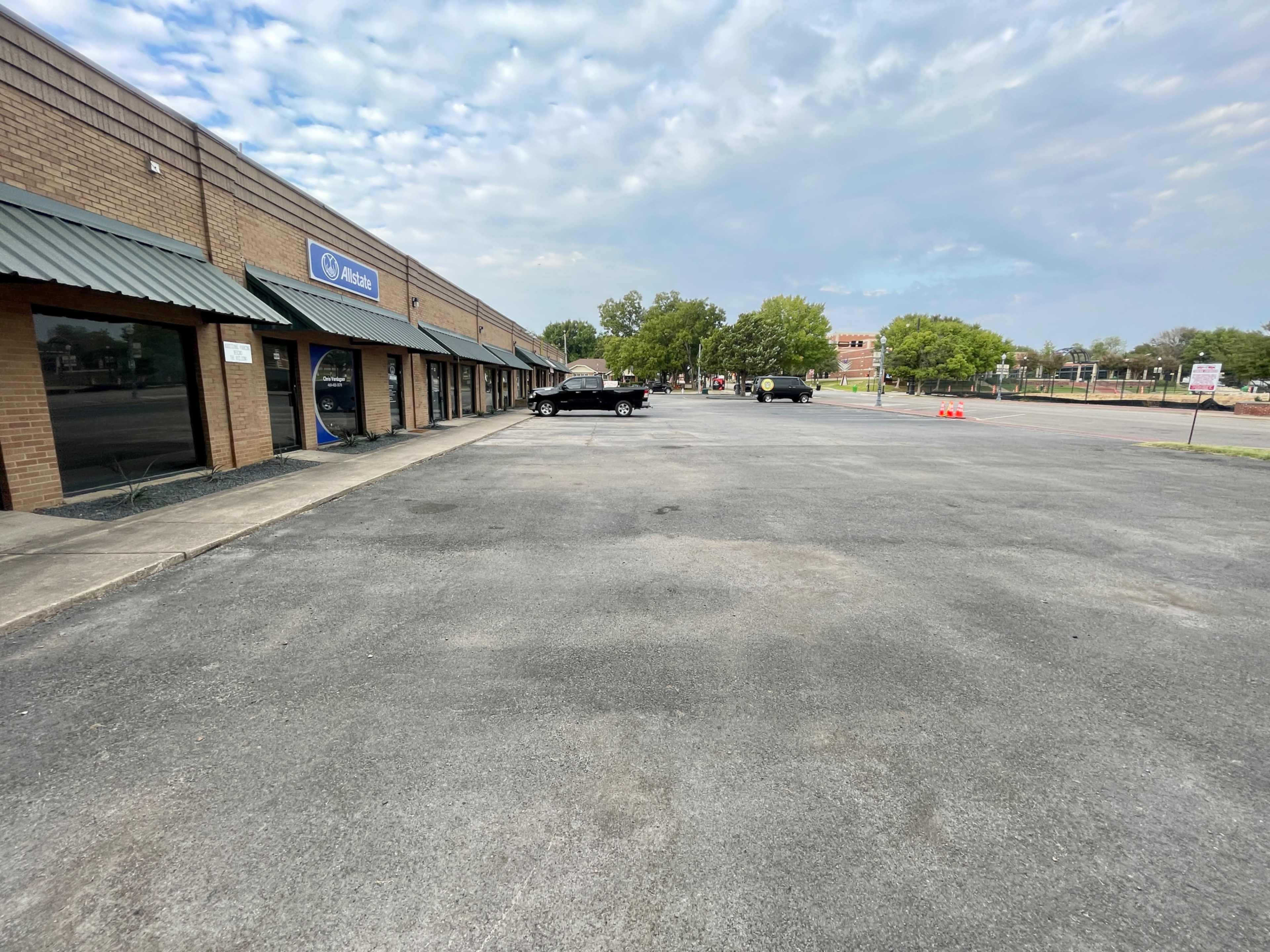 A parking lot in front of a retail building with several vehicles parked along the side.