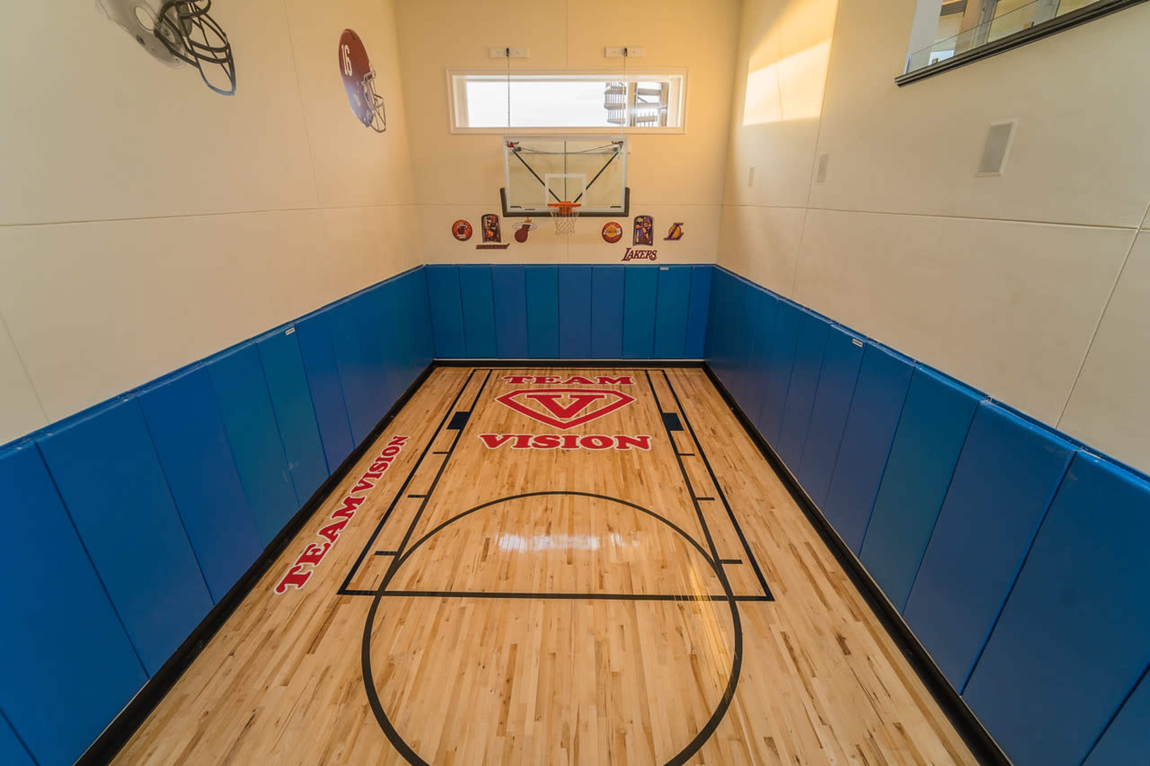 A small indoor basketball court with a wooden floor, wall-mounted hoop, and padded wall panels.