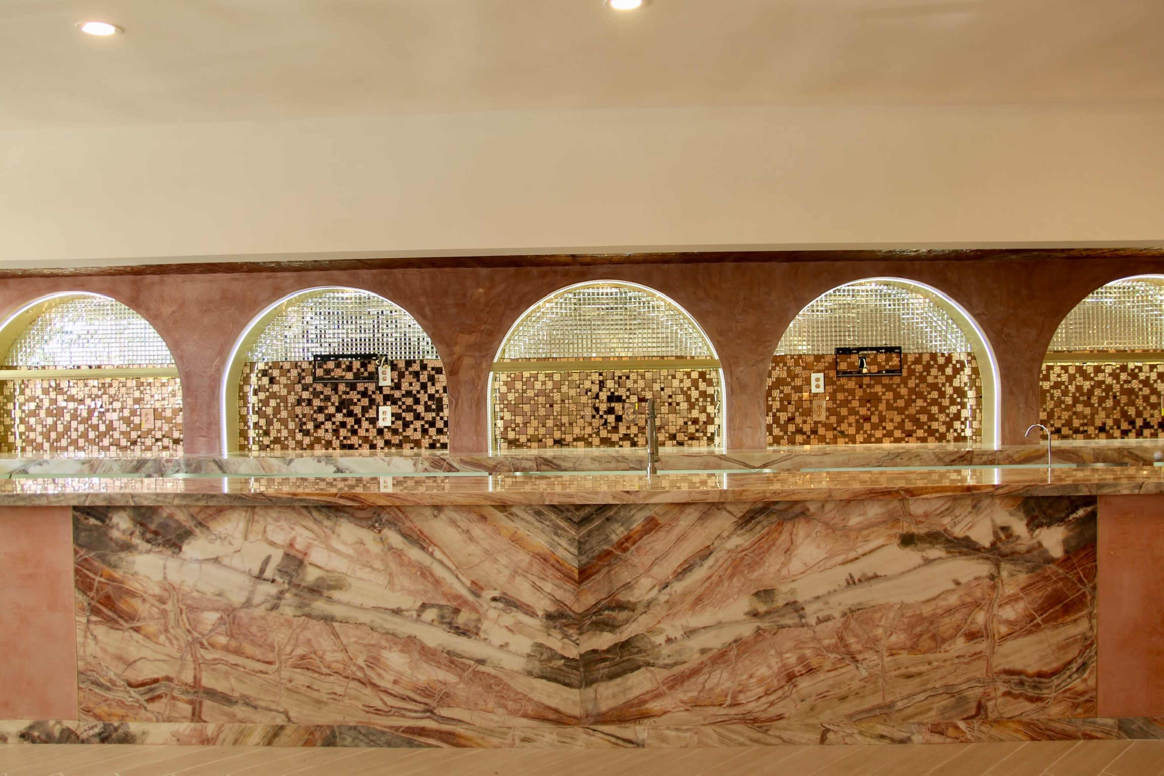 The image shows a sleek countertop made of marbled stone, featuring several arch-shaped openings in the back wall with decorative tiles.