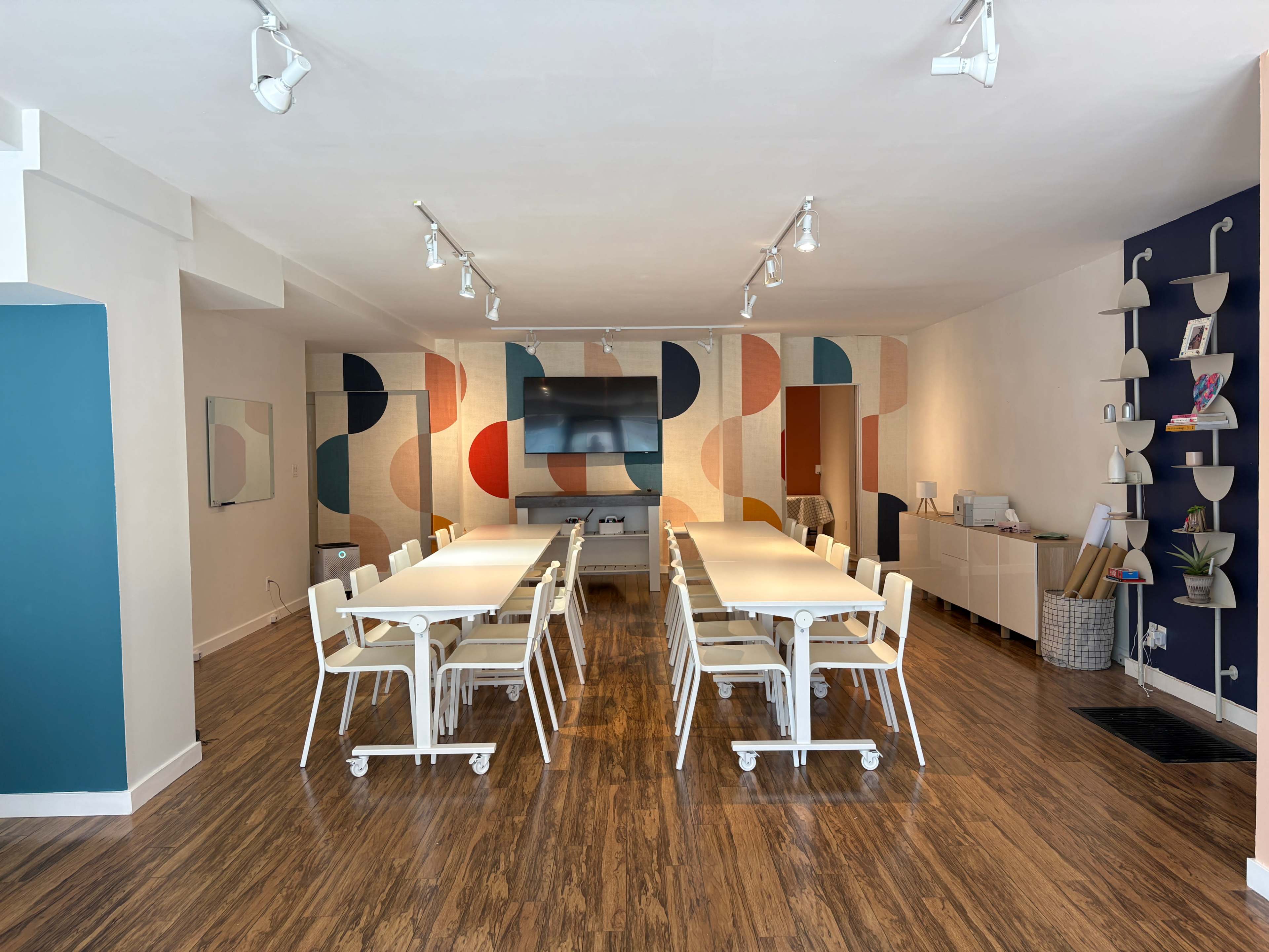 The image shows a spacious, modern meeting room with a long table surrounded by chairs, and colorful wall designs in the background.