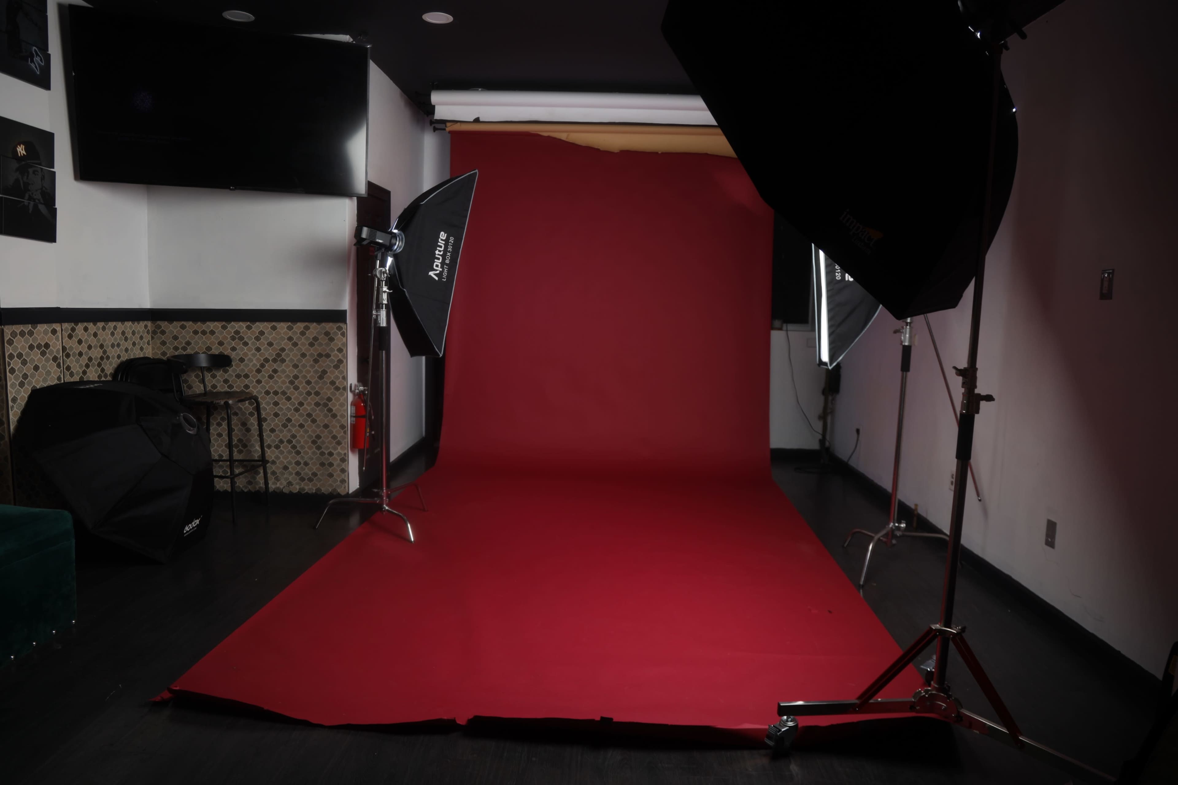A photography studio setup featuring a red backdrop, softbox lights, and a dark wooden floor.