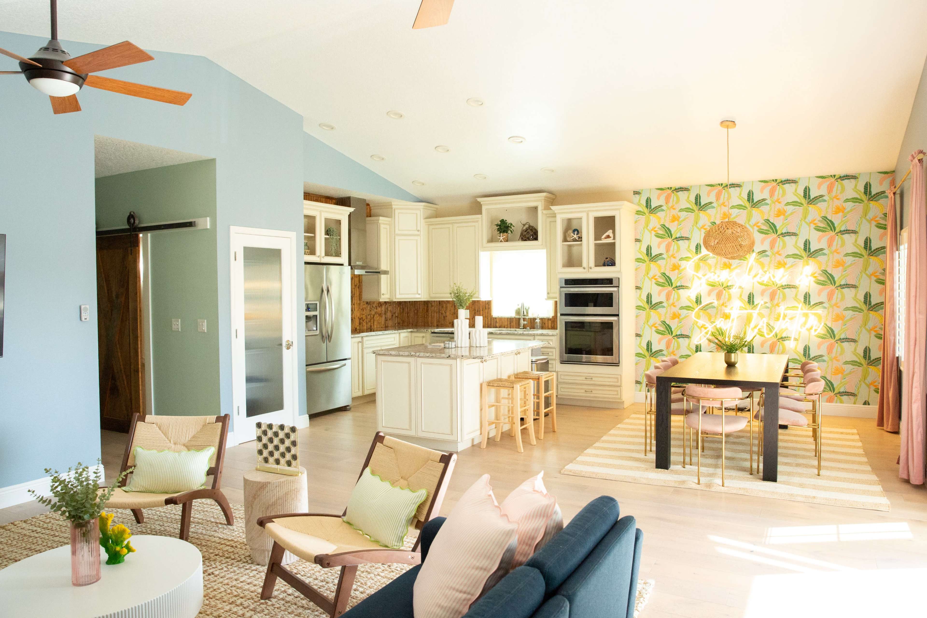 The open-concept kitchen and dining area features modern appliances and a tropical-themed wallpaper, with a dining table and comfortable seating arranged for casual gatherings.