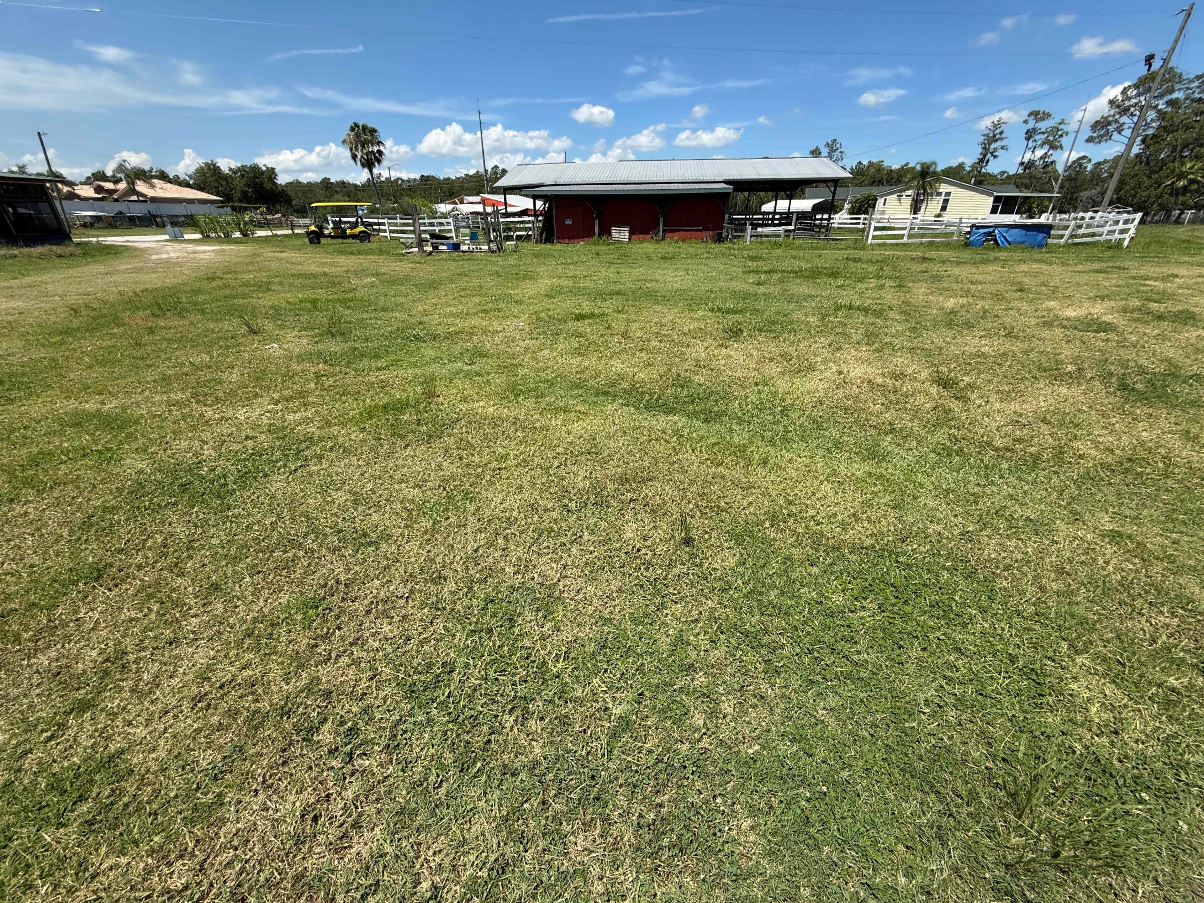 The image shows a wide, grassy field with a barn and several trees under a partly cloudy sky.