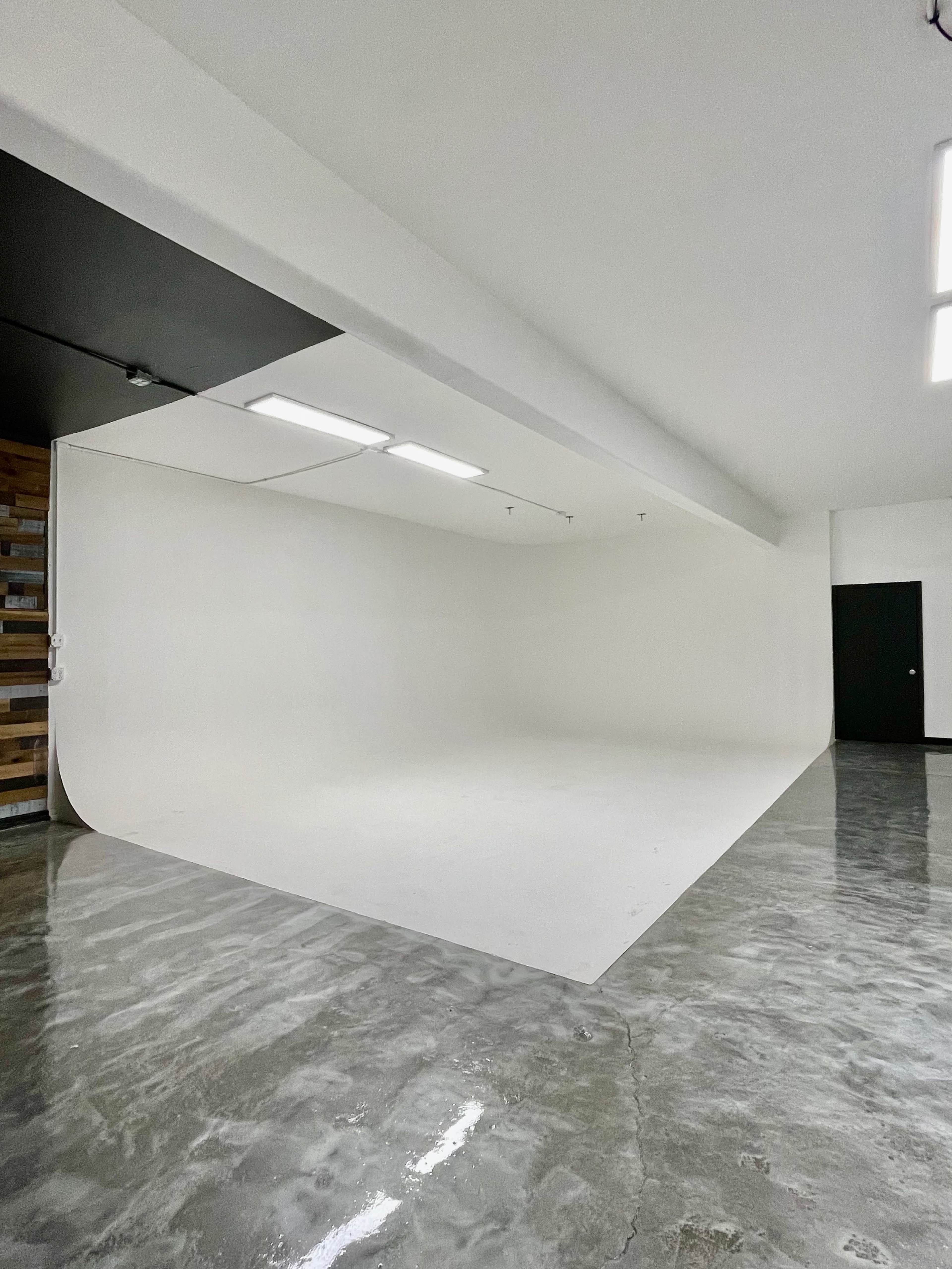 A spacious photography studio with a seamless white backdrop and polished concrete floors.