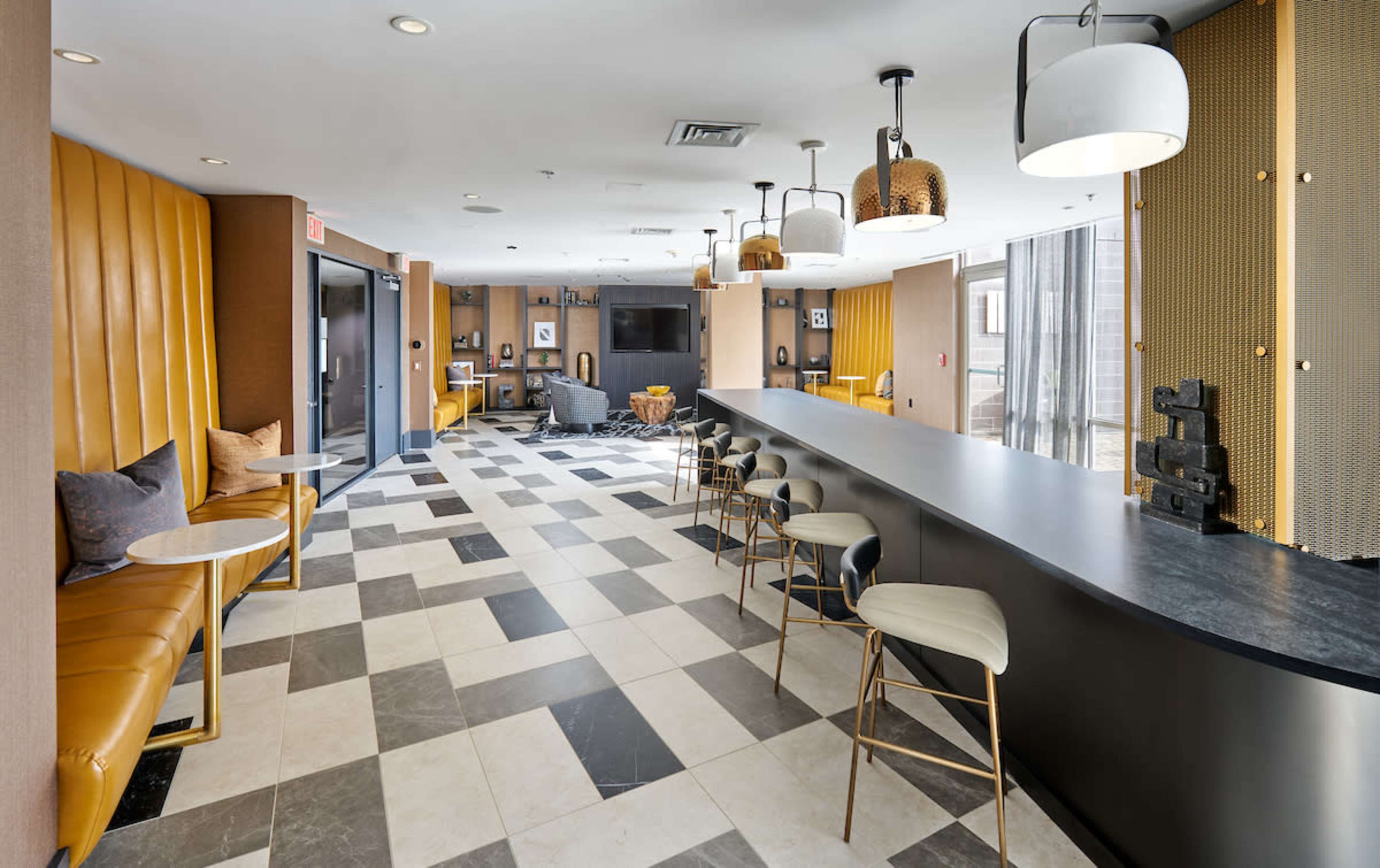 A modern lounge area with a bar, featuring a mix of black and white tiled flooring, brown leather seating, and stylish light fixtures.