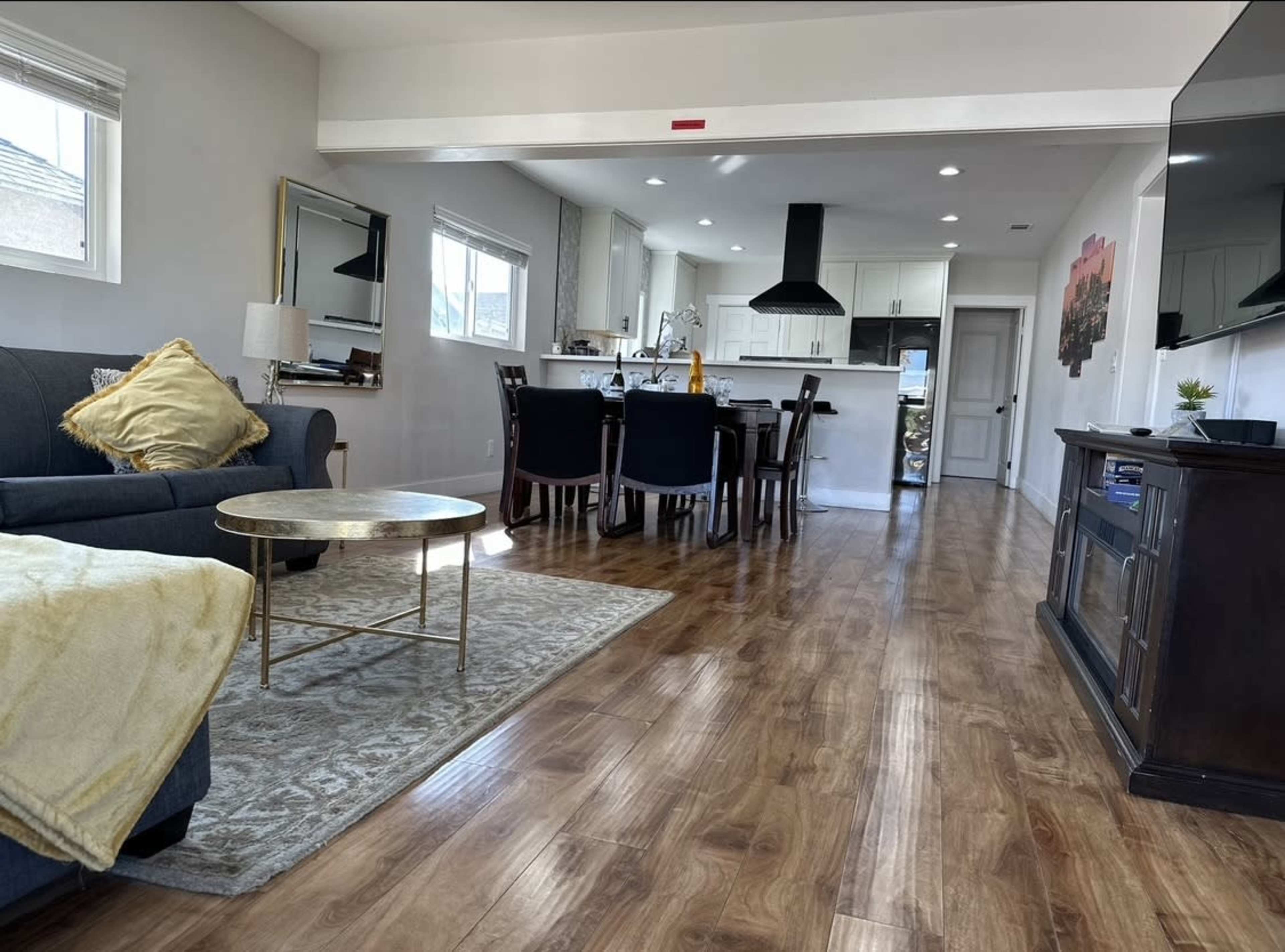 A living area features a sofa, coffee table, and a dining space with a kitchen in the background.